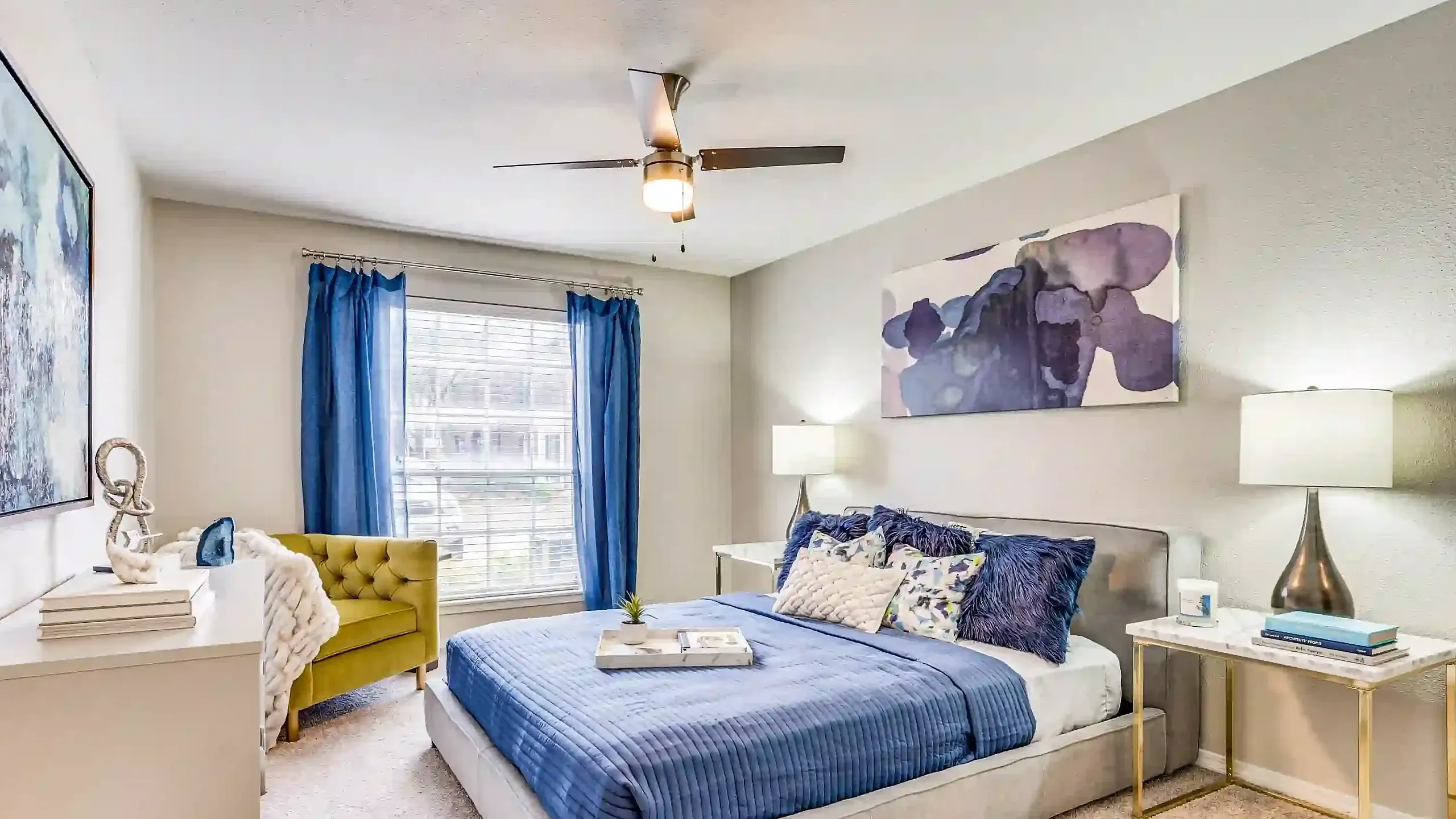 Bright and cozy bedroom featuring a stylish bed with blue accents, chic artwork, and elegant lighting for a serene living experience.