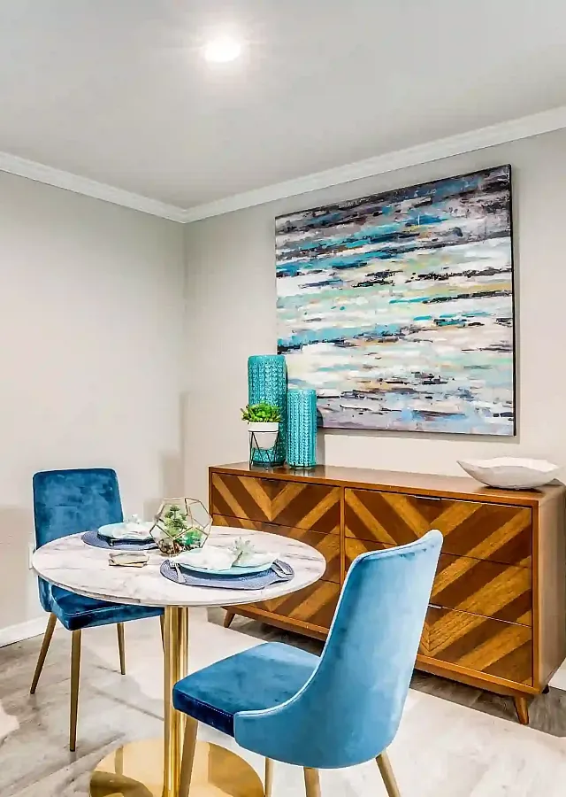 Chic dining nook with modern blue chairs, elegant wooden sideboard, and stylish wall art, creating a cozy and inviting ambiance.