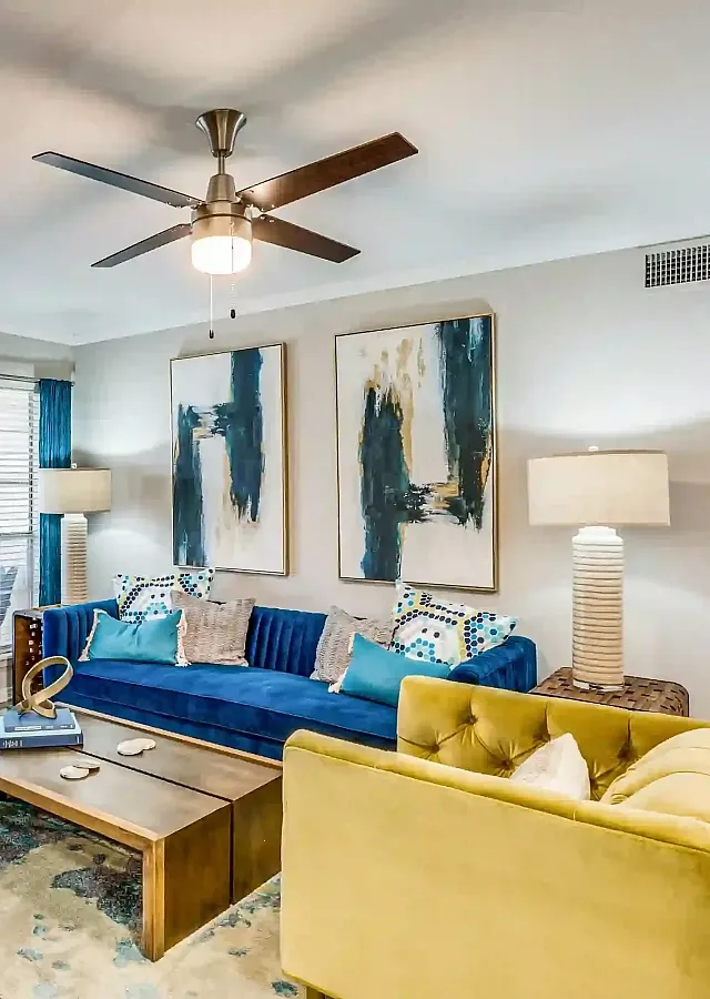 Elegant living room with modern art, stylish blue and yellow seating, and a cozy fireplace.