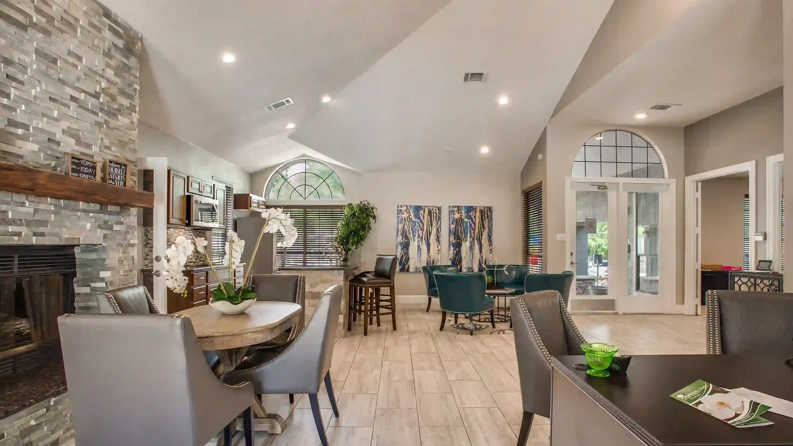 Elegant community clubhouse lounge featuring a stone fireplace, modern seating areas, dining tables, and vaulted ceilings.