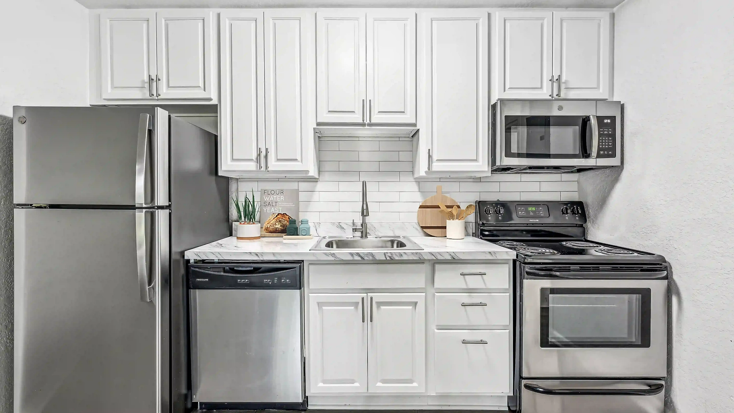 Modern apartment kitchen featuring white cabinetry, marble-look countertops, subway tile backsplash, and stainless steel appliances.