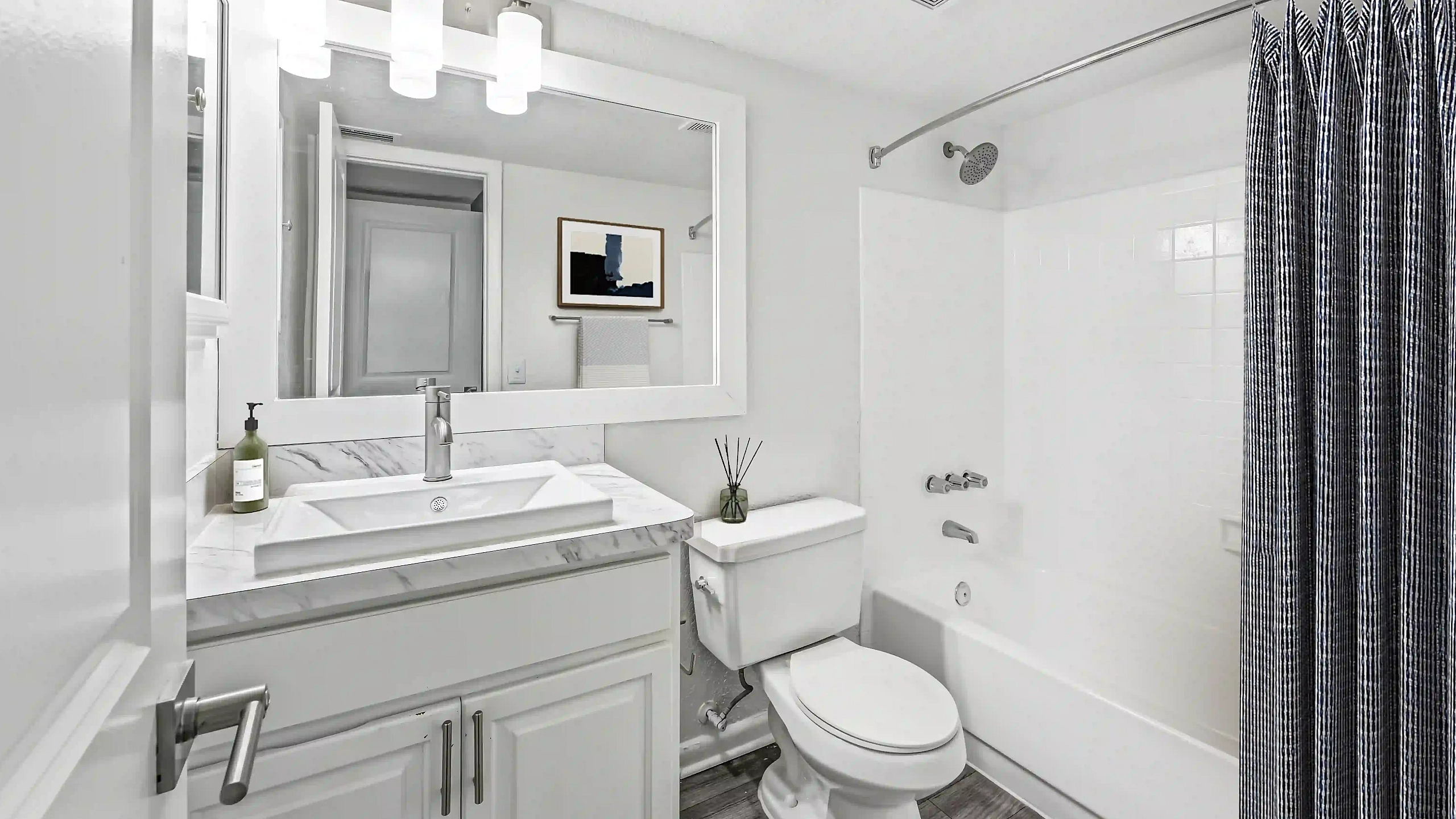 Modern apartment bathroom featuring a white vanity with marble-look countertop, large framed mirror, and bathtub with shower and striped curtain.