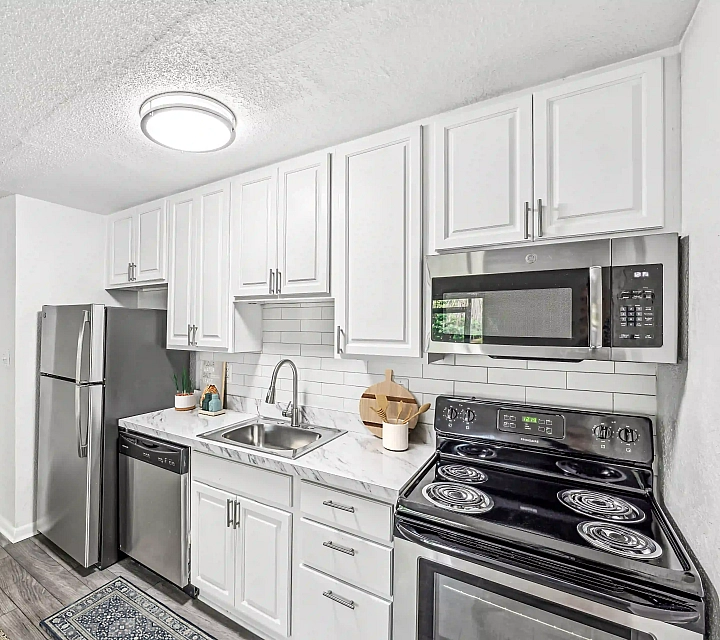 Modern apartment kitchen featuring white cabinetry, marble-look countertops, subway tile backsplash, stainless steel appliances, and wood-look flooring.
