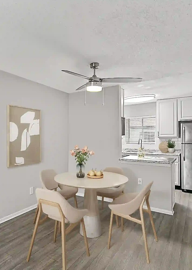 Modern apartment dining area featuring a round table with four chairs, ceiling fan, wood-look flooring, an open kitchen with stainless steel appliances, and a stacked washer and dryer.
