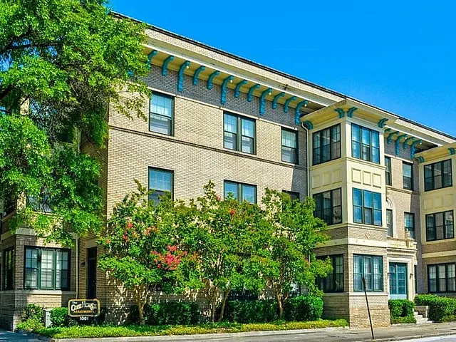 Charming historic apartment building with elegant architectural details surrounded by lush greenery under a clear blue sky.