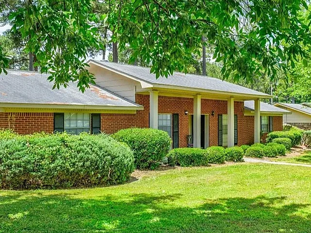 Charming red-brick apartment surrounded by lush greenery and mature trees, offering a serene and inviting atmosphere.