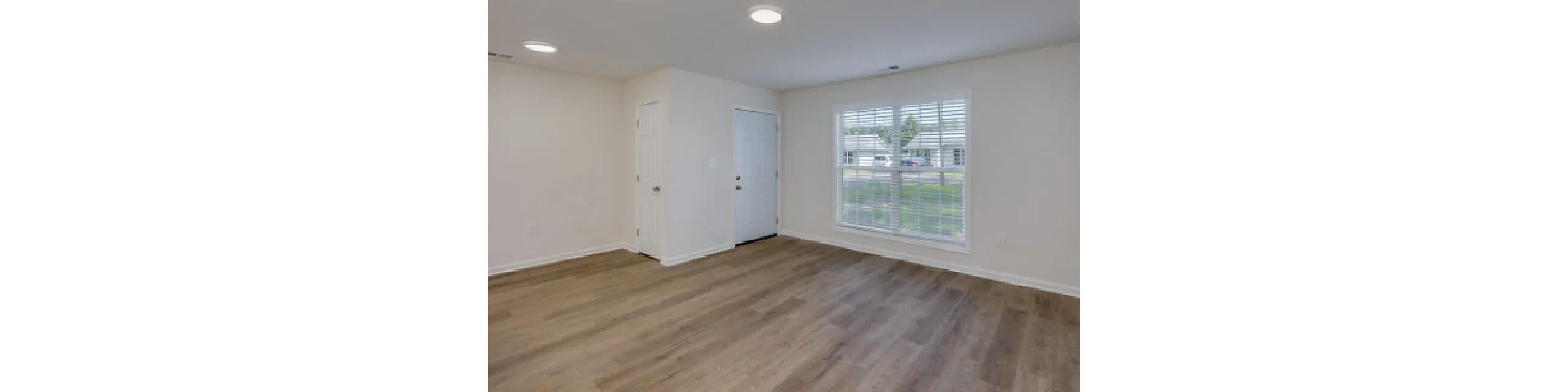 Spacious living room with large window and elegant wood flooring.