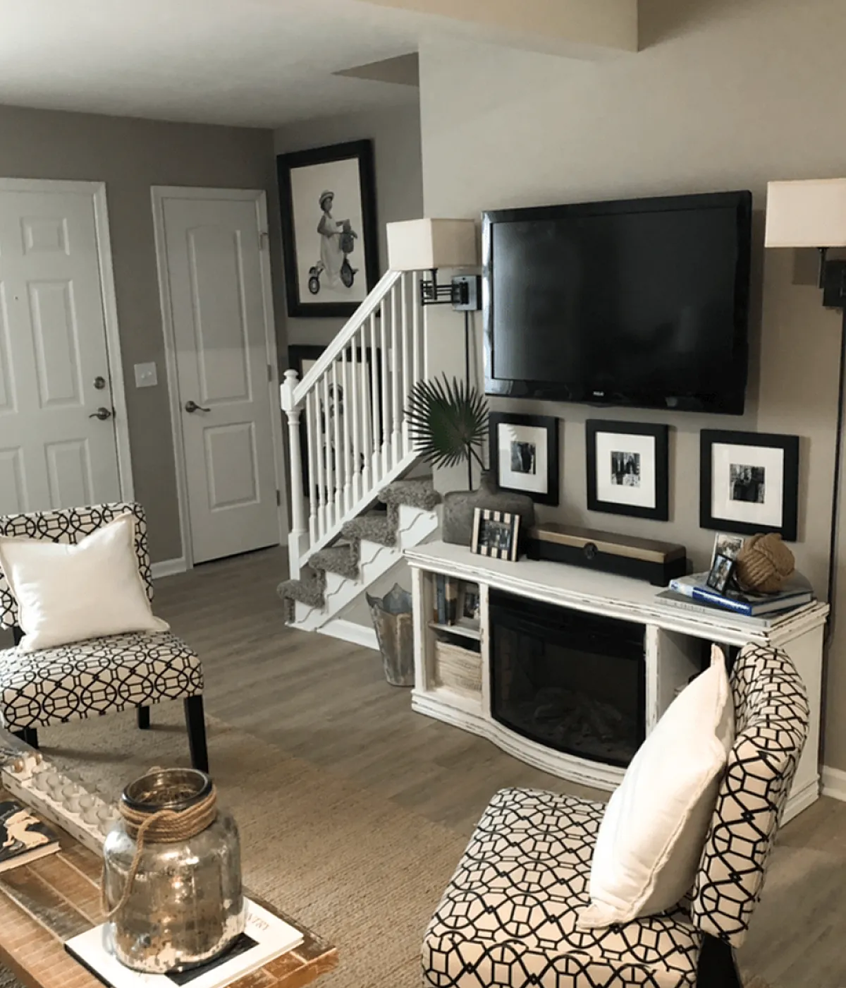 Charming living room with modern decor, featuring patterned chairs, a cozy fireplace, and a wall-mounted TV near a stylish staircase.