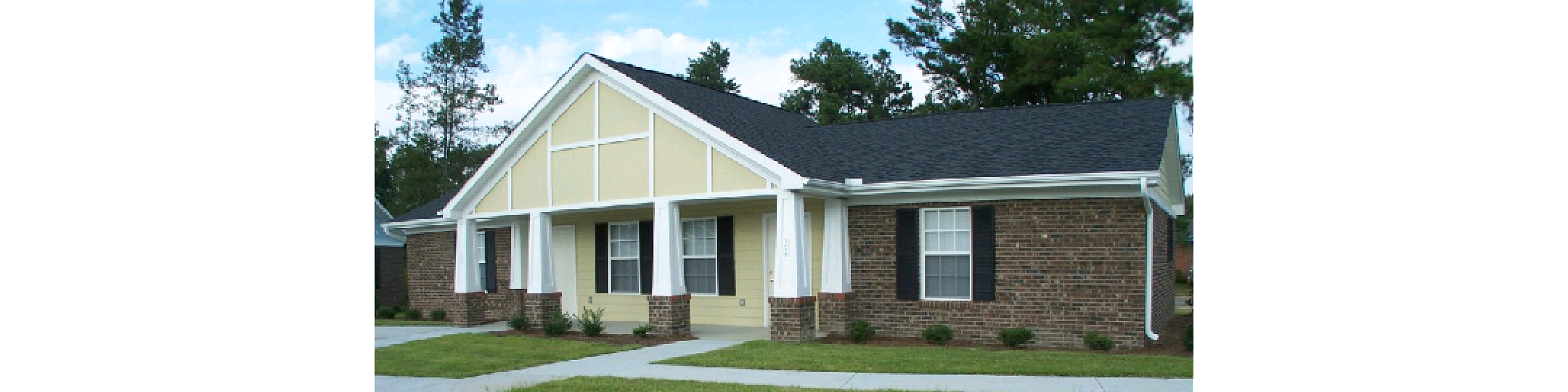 Charming single-story brick house with elegant white columns, a neatly manicured lawn, and surrounded by lush trees.
