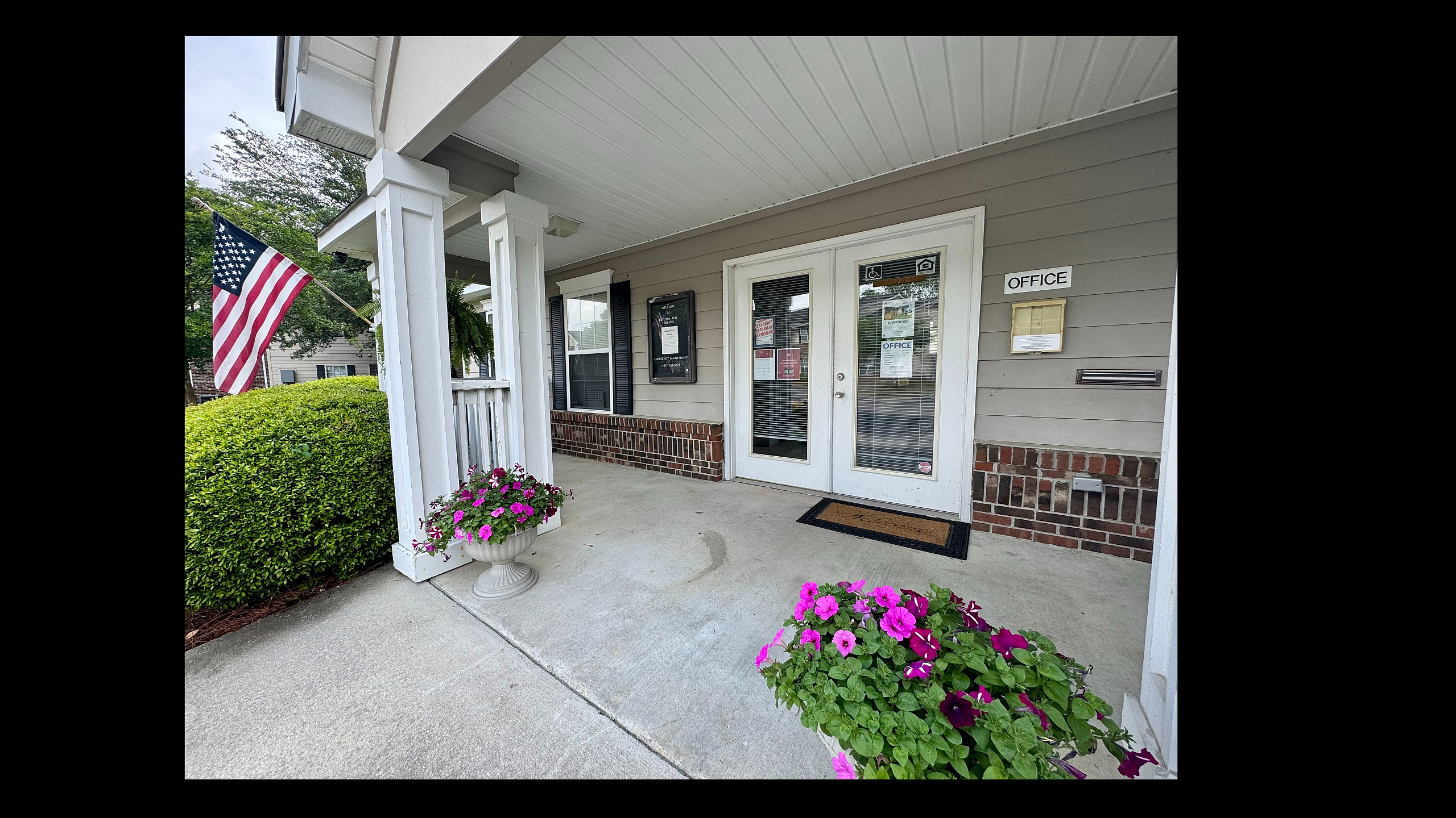 Welcoming apartment office entrance with vibrant flowers, American flag, and elegant architectural details.