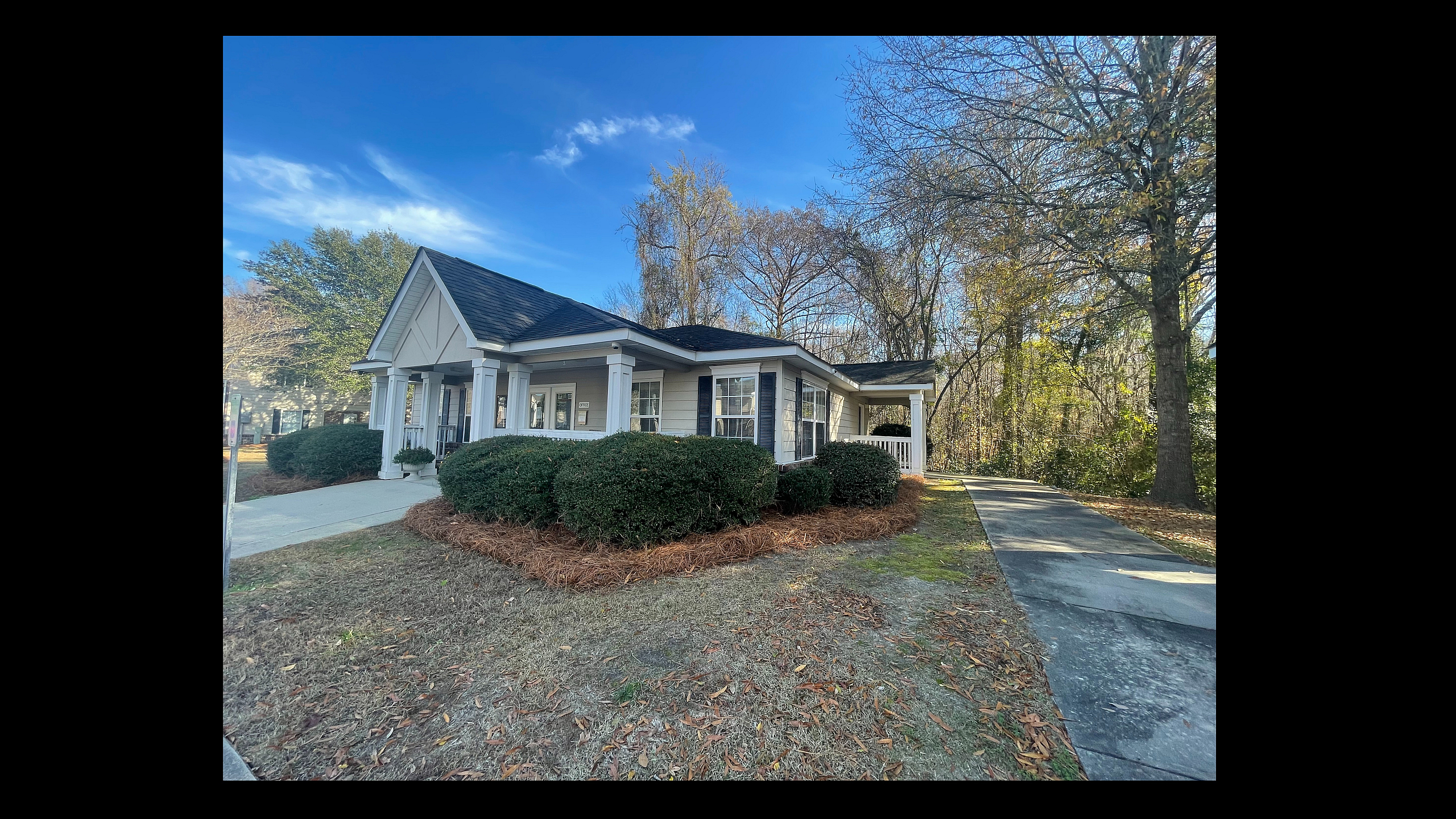 Charming single-story house with inviting porch, nestled in a serene setting surrounded by lush trees and manicured hedges.