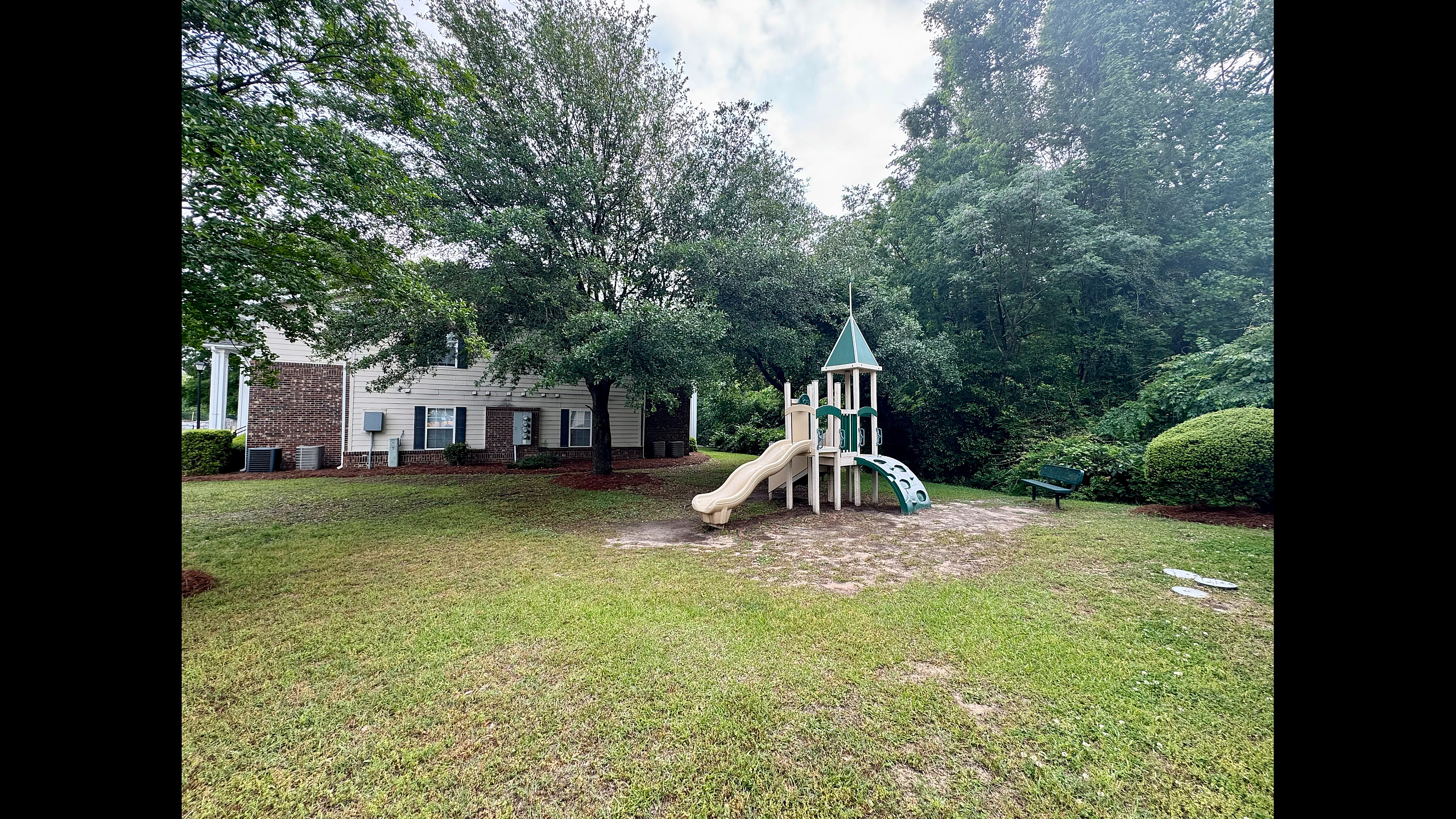 Charming outdoor playground nestled in a serene green landscape, adjacent to a brick-faced family home.