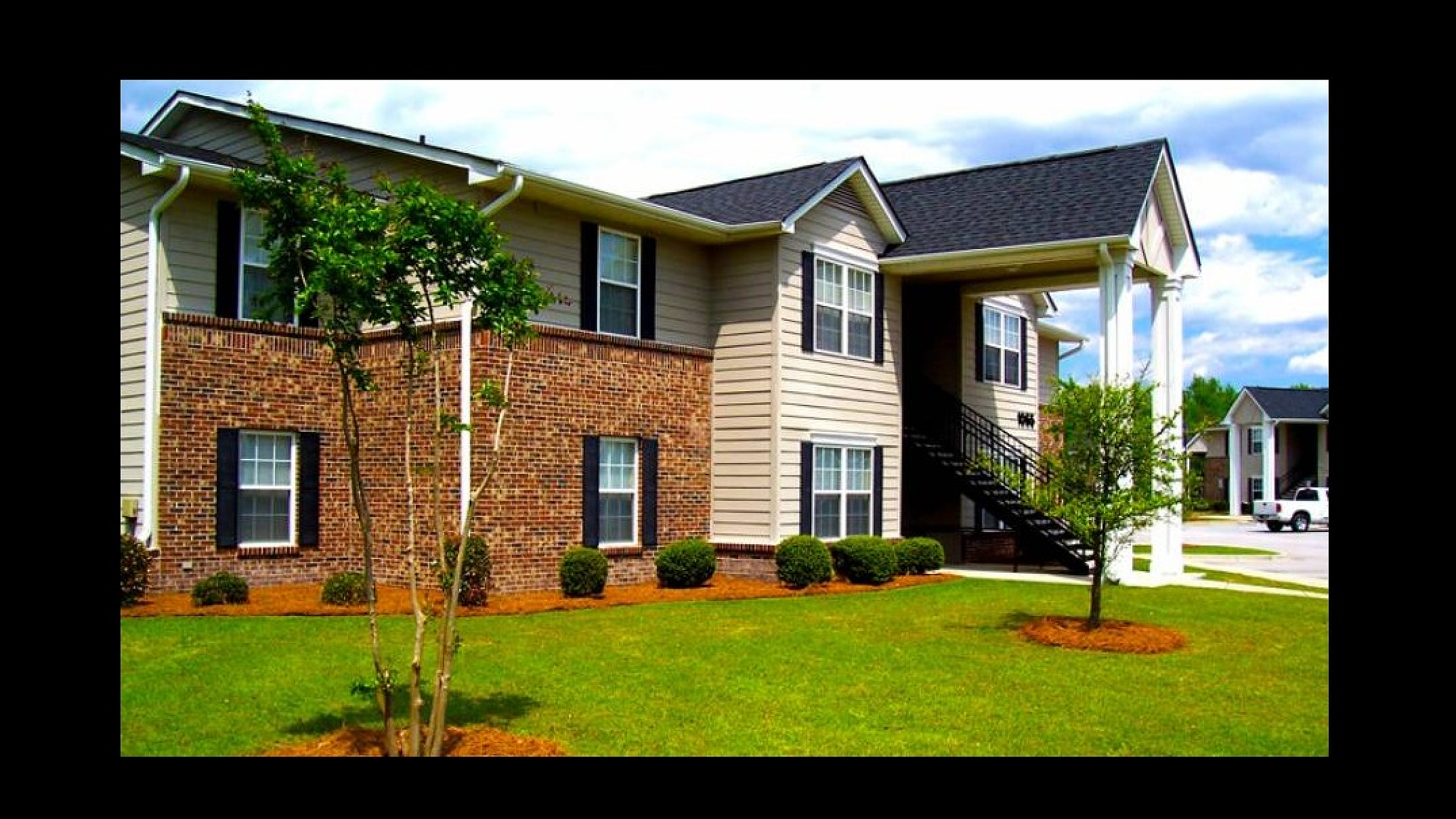 Charming two-story apartment building with a brick facade, lush green lawn, and elegant front steps.