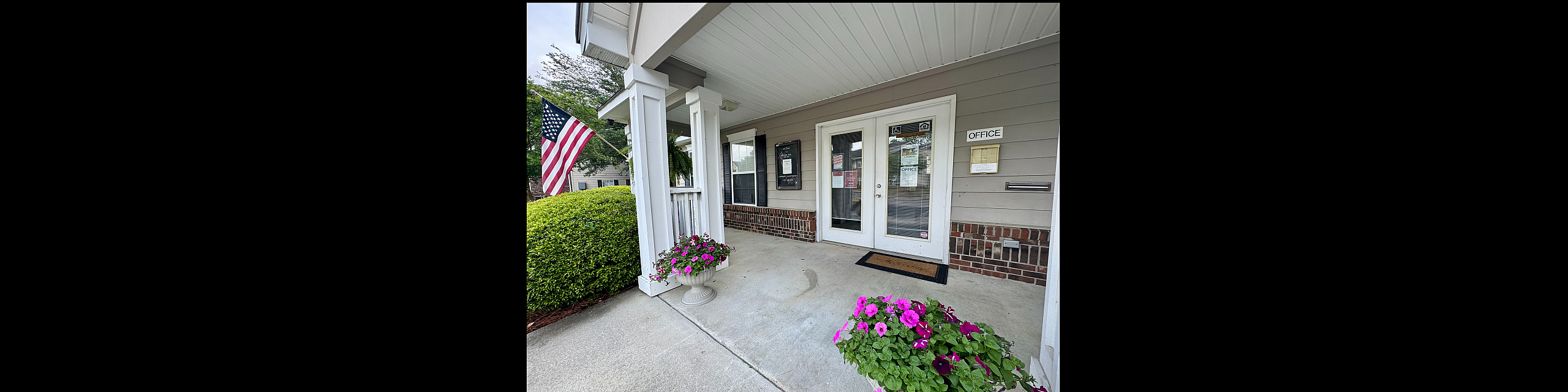 Charming apartment entrance with lush greenery, vibrant flowers, and welcoming office space.