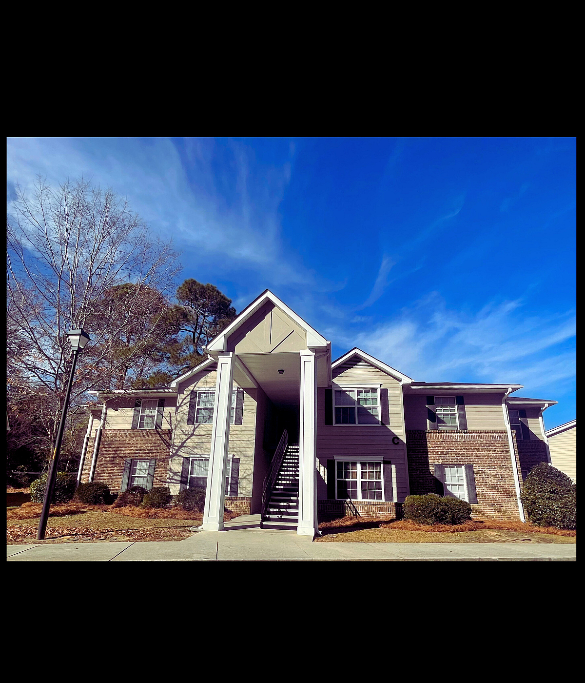 Charming apartment complex with brick and siding exterior, surrounded by trees and a bright blue sky.