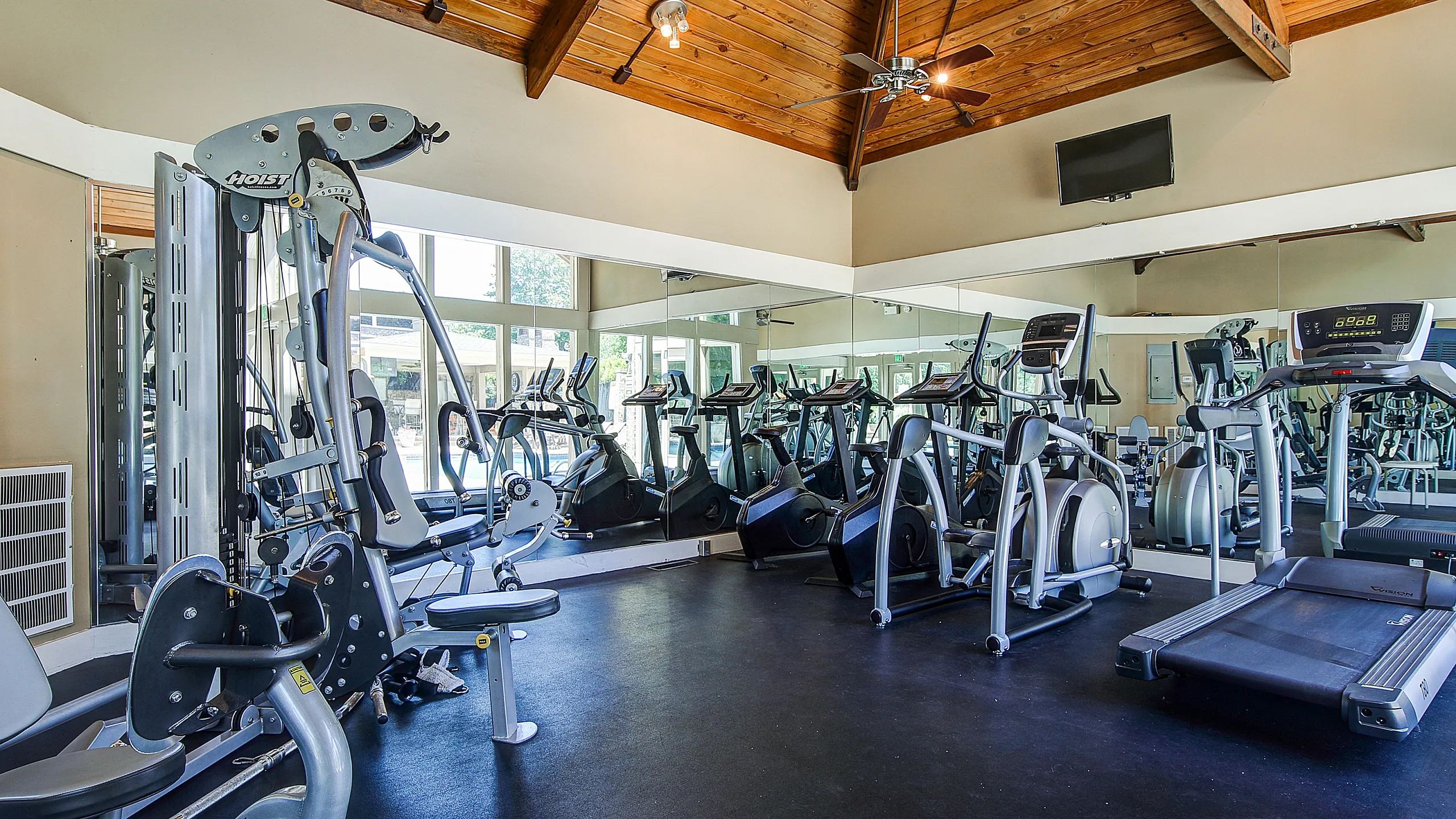 Modern fitness center with state-of-the-art exercise equipment, mirrored walls, and high wooden ceilings for an invigorating workout experience.