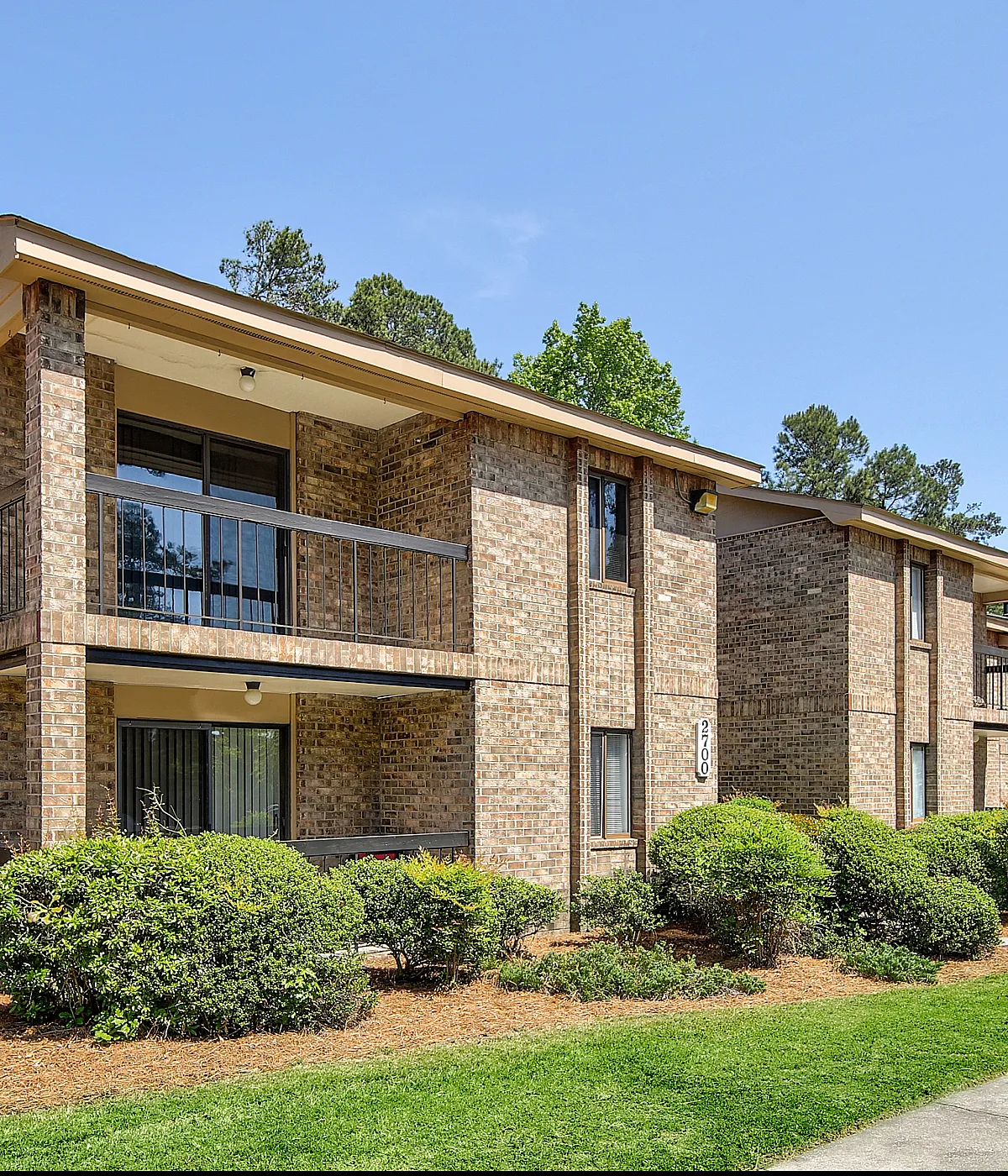Charming brick apartment complex with spacious balconies and lush landscaping, perfect for serene living.