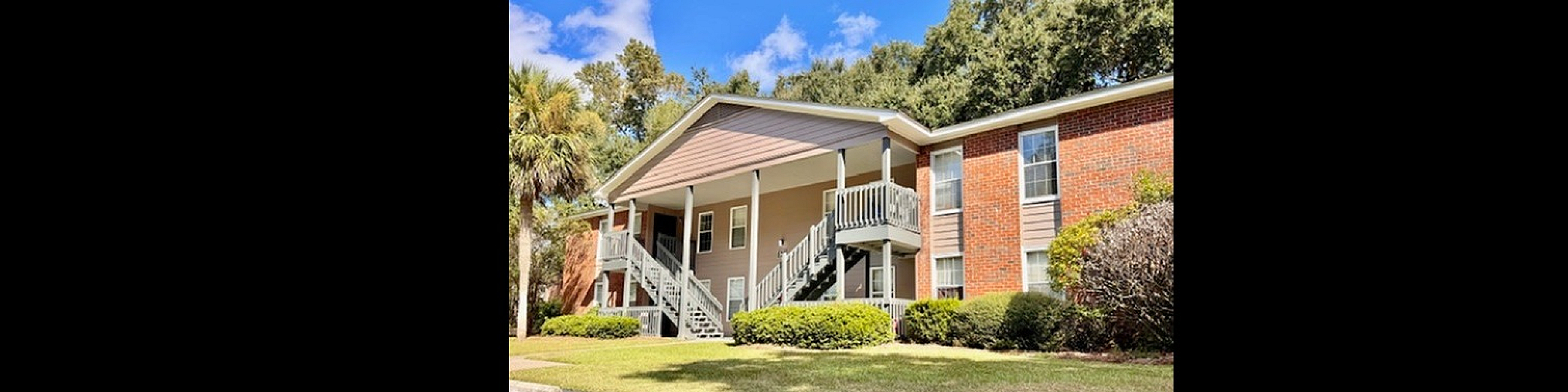 Charming two-story apartment building with inviting balconies, lush greenery, and ample parking in a serene neighborhood.