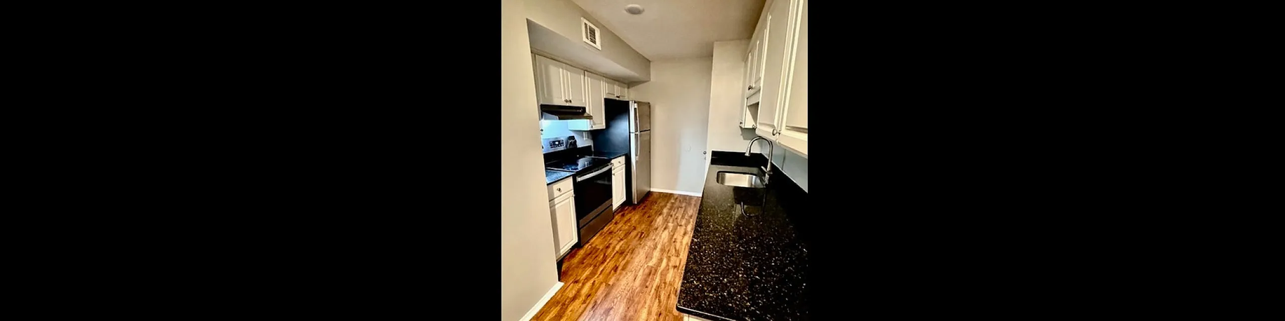 Elegant kitchen with sleek black granite countertops, stainless steel appliances, and warm wooden flooring.