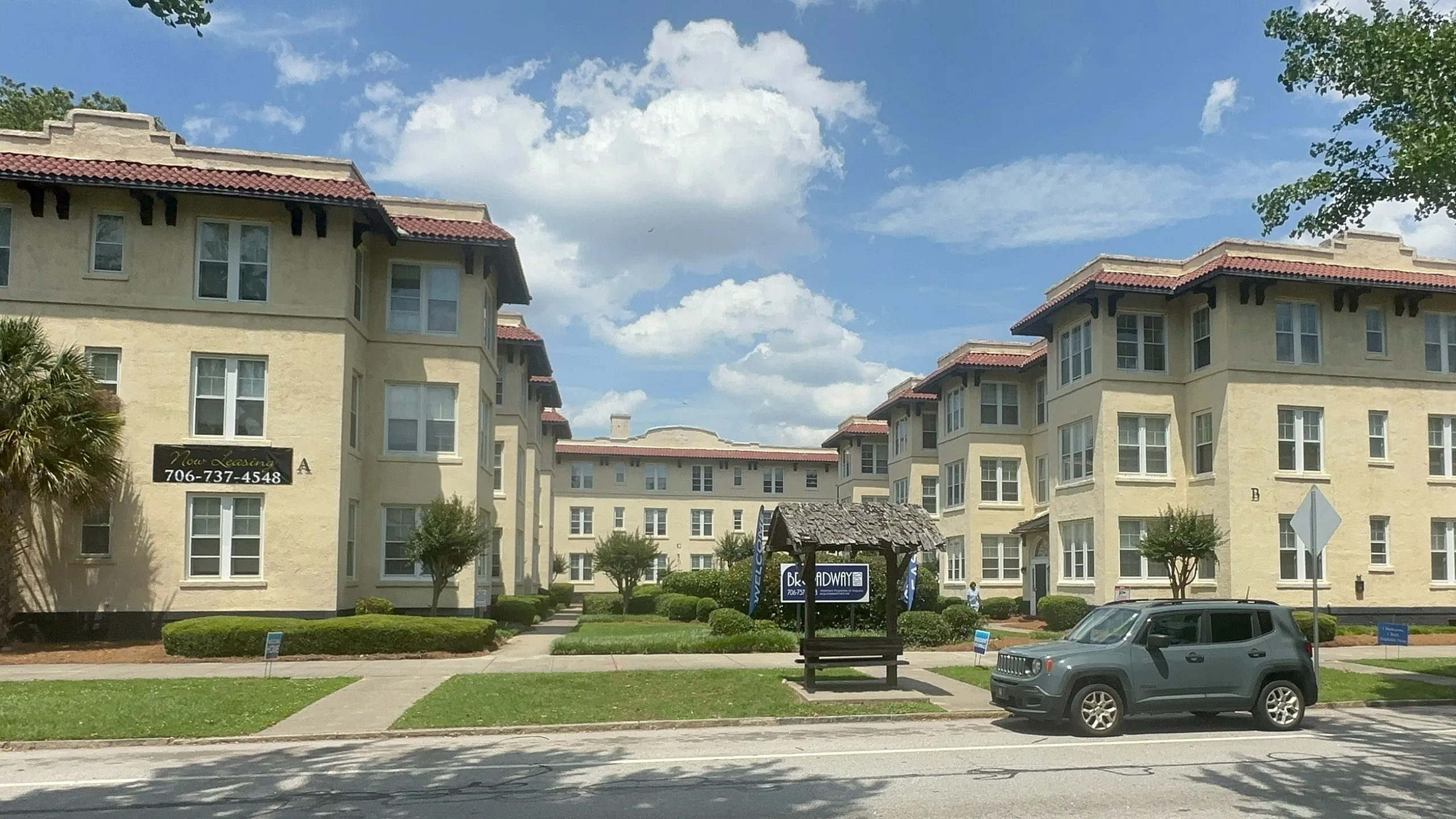 Charming apartment complex with stylish stucco exterior, surrounded by lush greenery, under a bright blue sky.