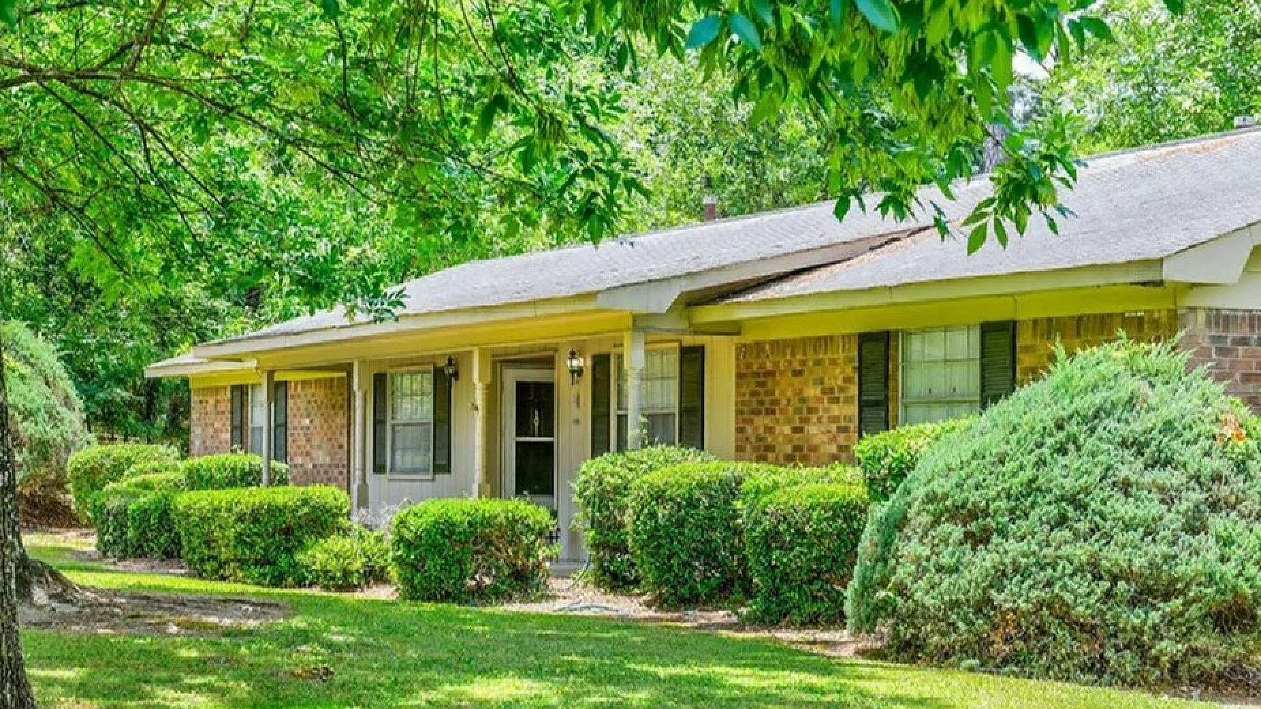 Charming brick house with lush, green landscaping and inviting porch, surrounded by mature trees.