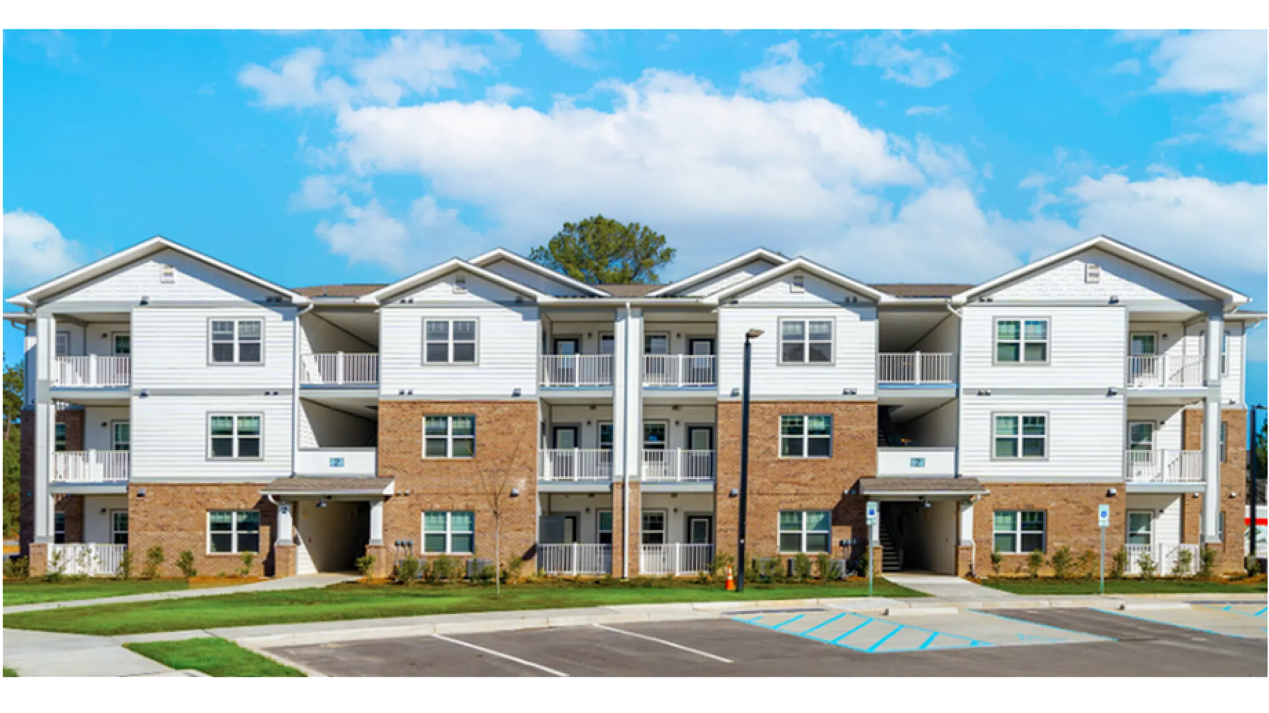 Charming modern apartment complex with three stories, featuring elegant balconies and a well-maintained parking area, set against a blue sky.