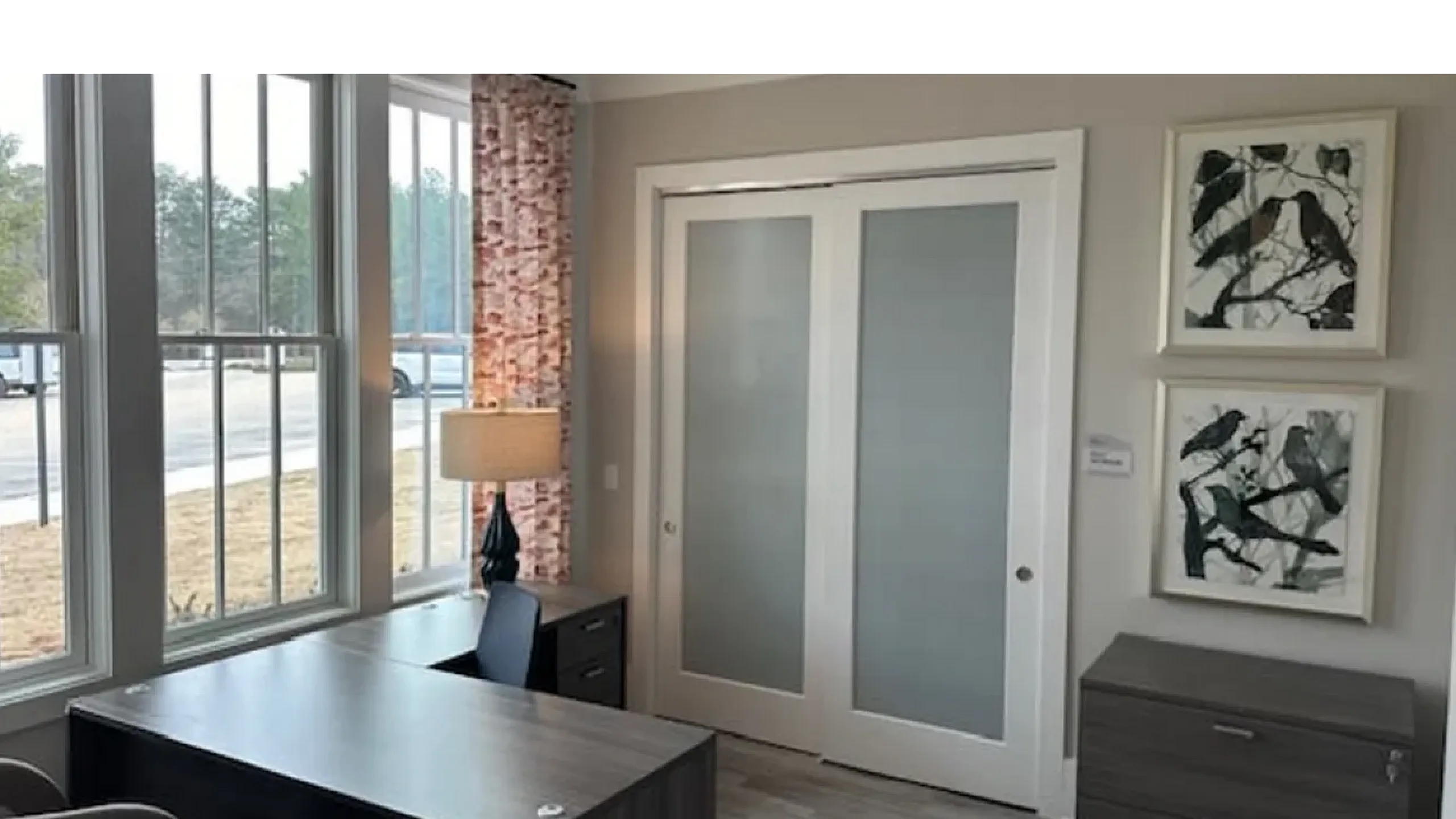 Bright home office with large windows, modern desk, and artistic wall decor.