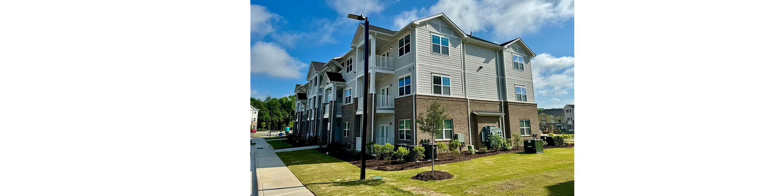 Charming three-story apartment complex with modern design, surrounded by lush greenery under a vibrant blue sky.