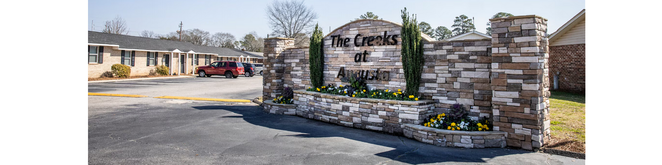 Inviting entrance of The Creeks at Augusta showcasing beautiful stonework and vibrant landscaping under a clear blue sky.
