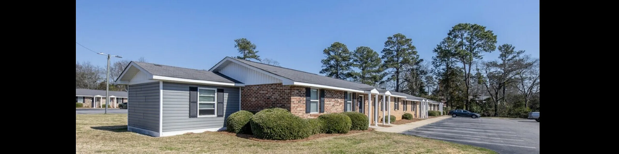Charming single-story apartment complex with brick and siding exterior, nestled in a serene suburban setting with ample parking and manicured landscaping.