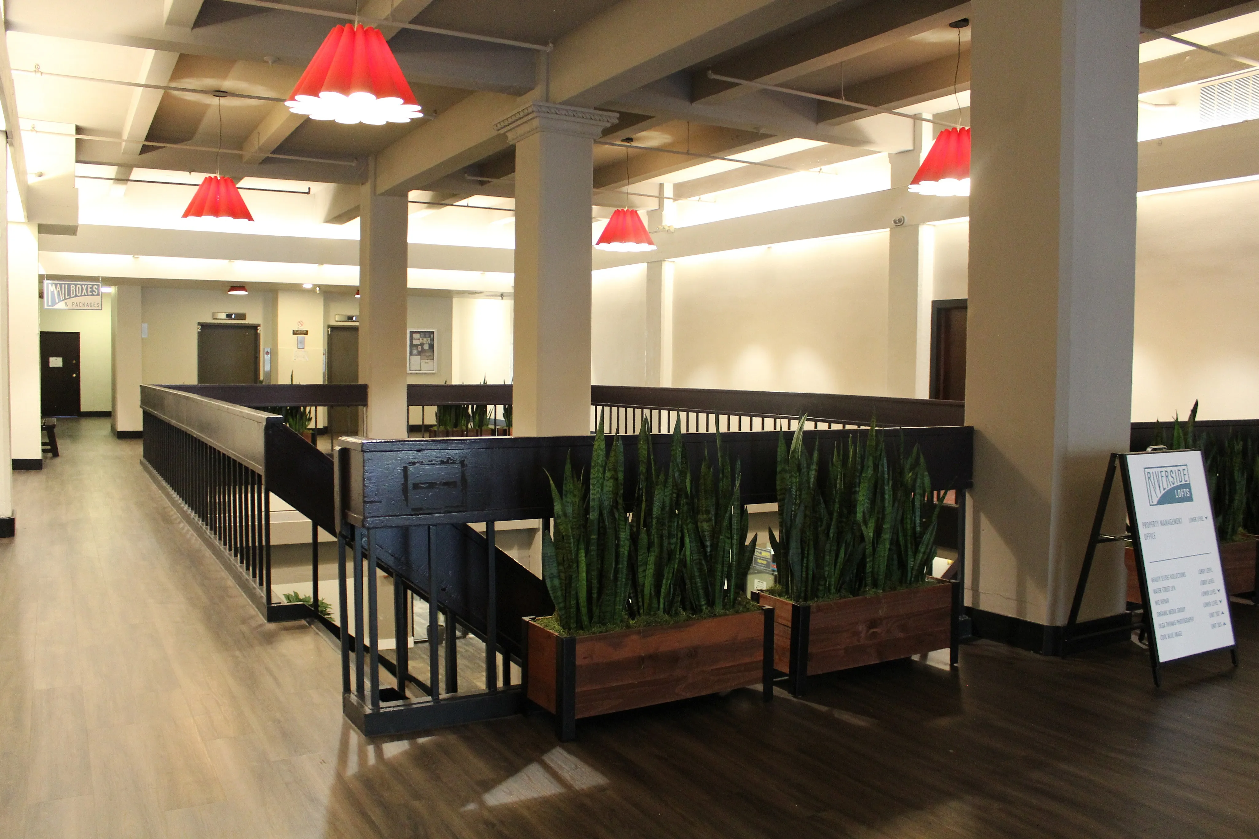 Modern apartment lobby with stylish red pendant lighting, sleek wood flooring, and lush potted plants, creating a welcoming ambiance.