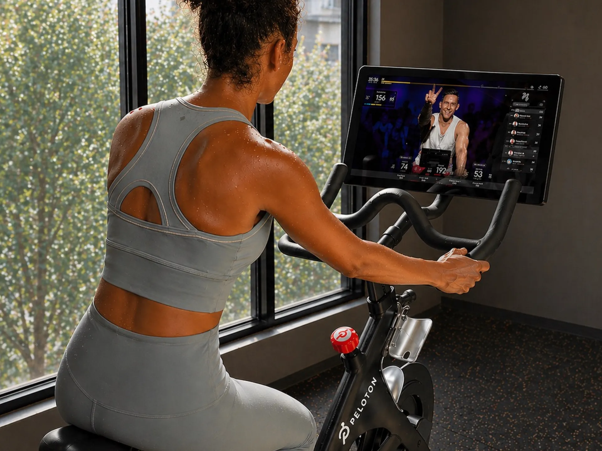 Motivated woman enjoying a high-energy cycling workout on a Peloton bike, engaging with an interactive screen in a bright, modern fitness space.