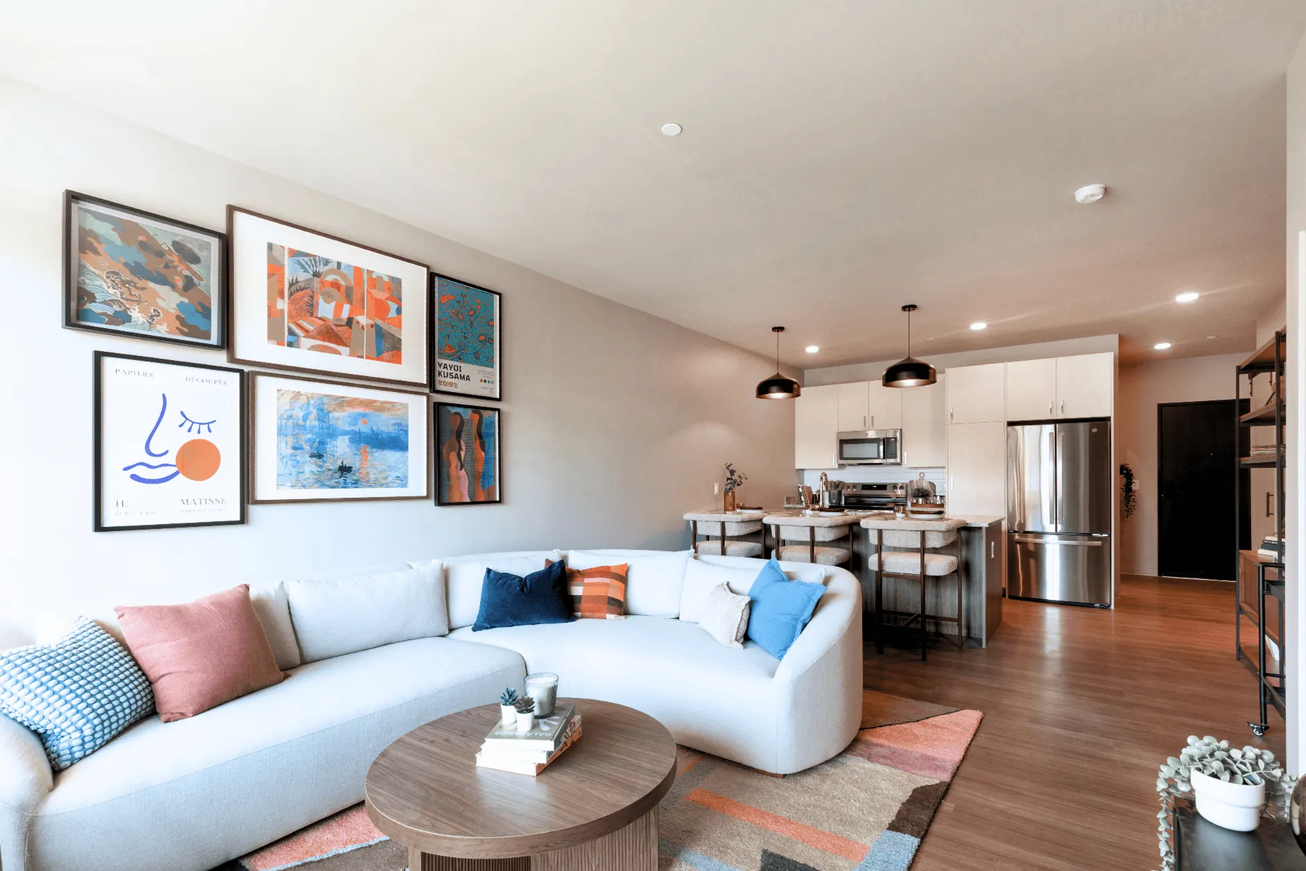 Modern open-concept living room with stylish decor, featuring a chic sectional sofa, vibrant artwork, and a sleek kitchen area with stainless steel appliances.