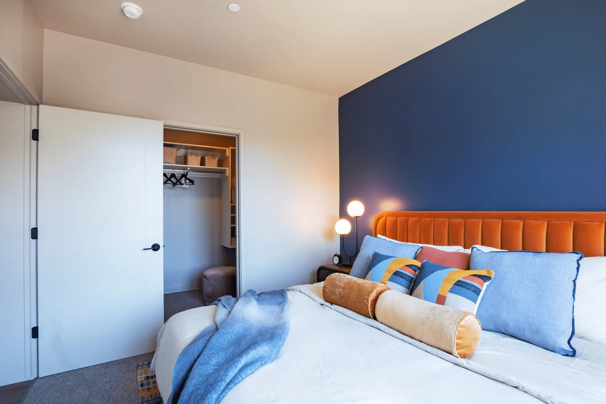 Bright and inviting bedroom with a plush orange headboard, cozy pillows, and a modern blue accent wall, leading to a spacious walk-in closet.