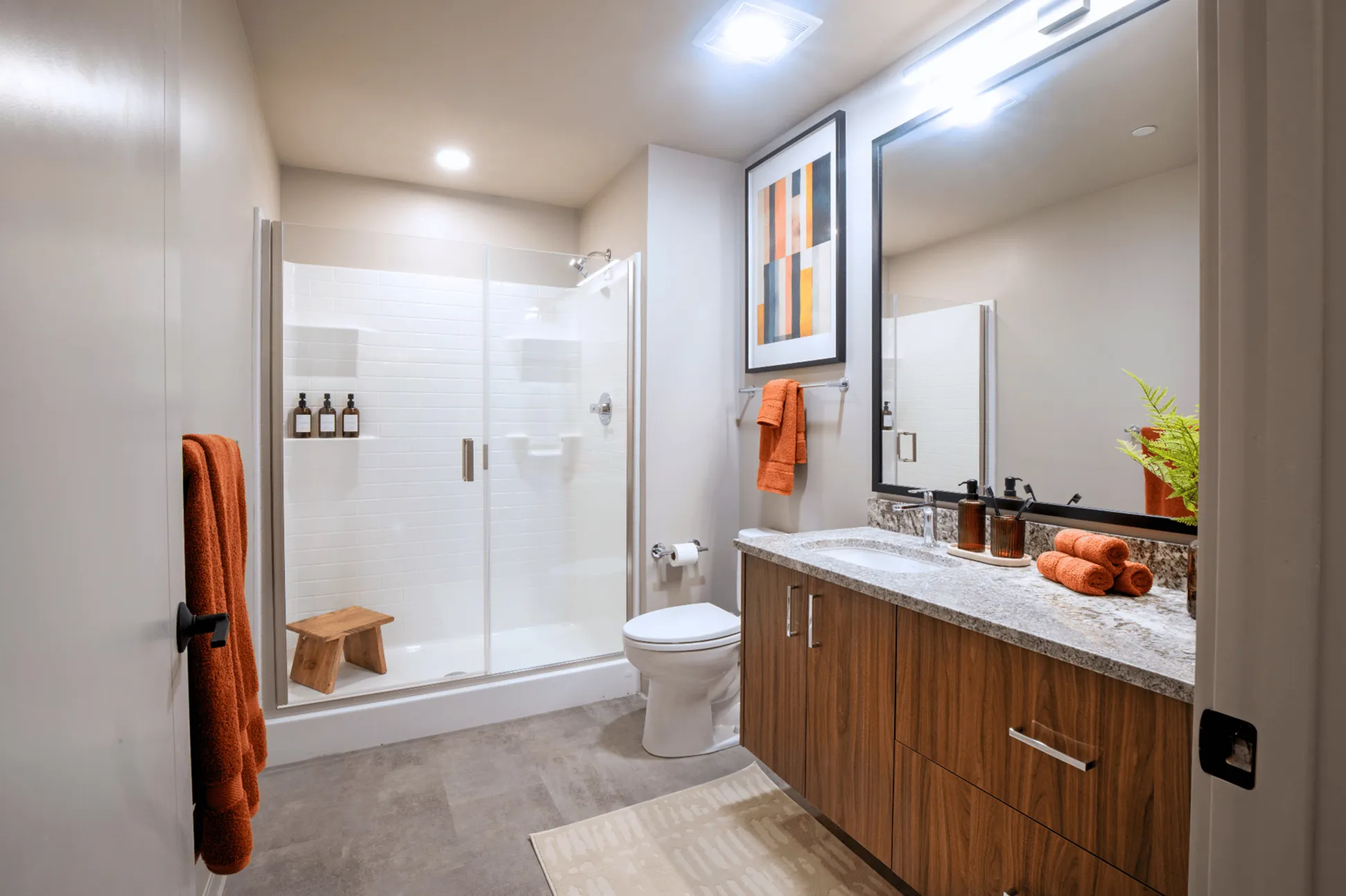 Modern bathroom featuring sleek wood cabinetry, elegant glass shower, and warm orange accents, creating a stylish and inviting space.