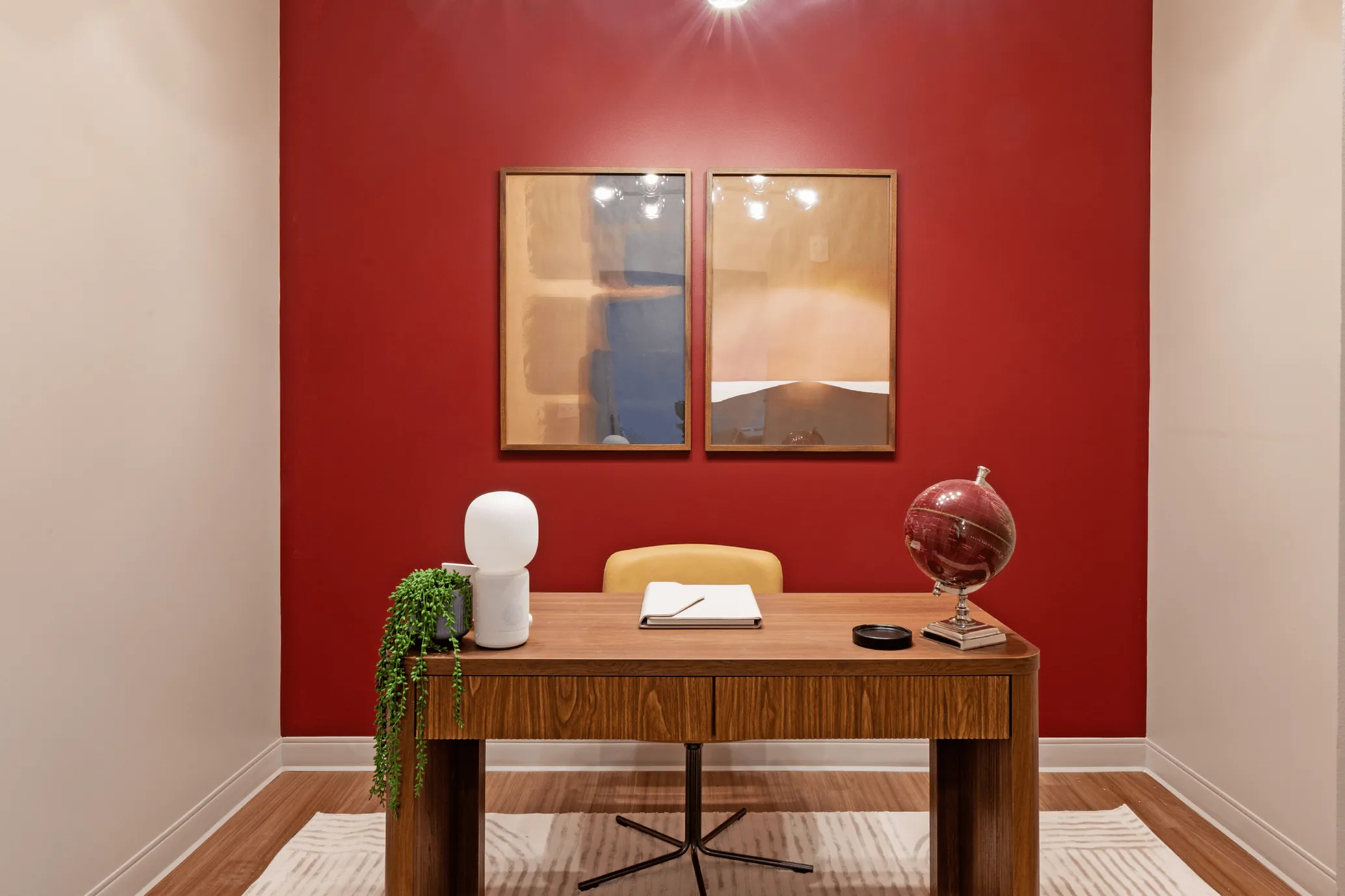 Chic home office featuring a stylish wood desk, vibrant red accent wall, and modern decor elements including a globe and abstract art.