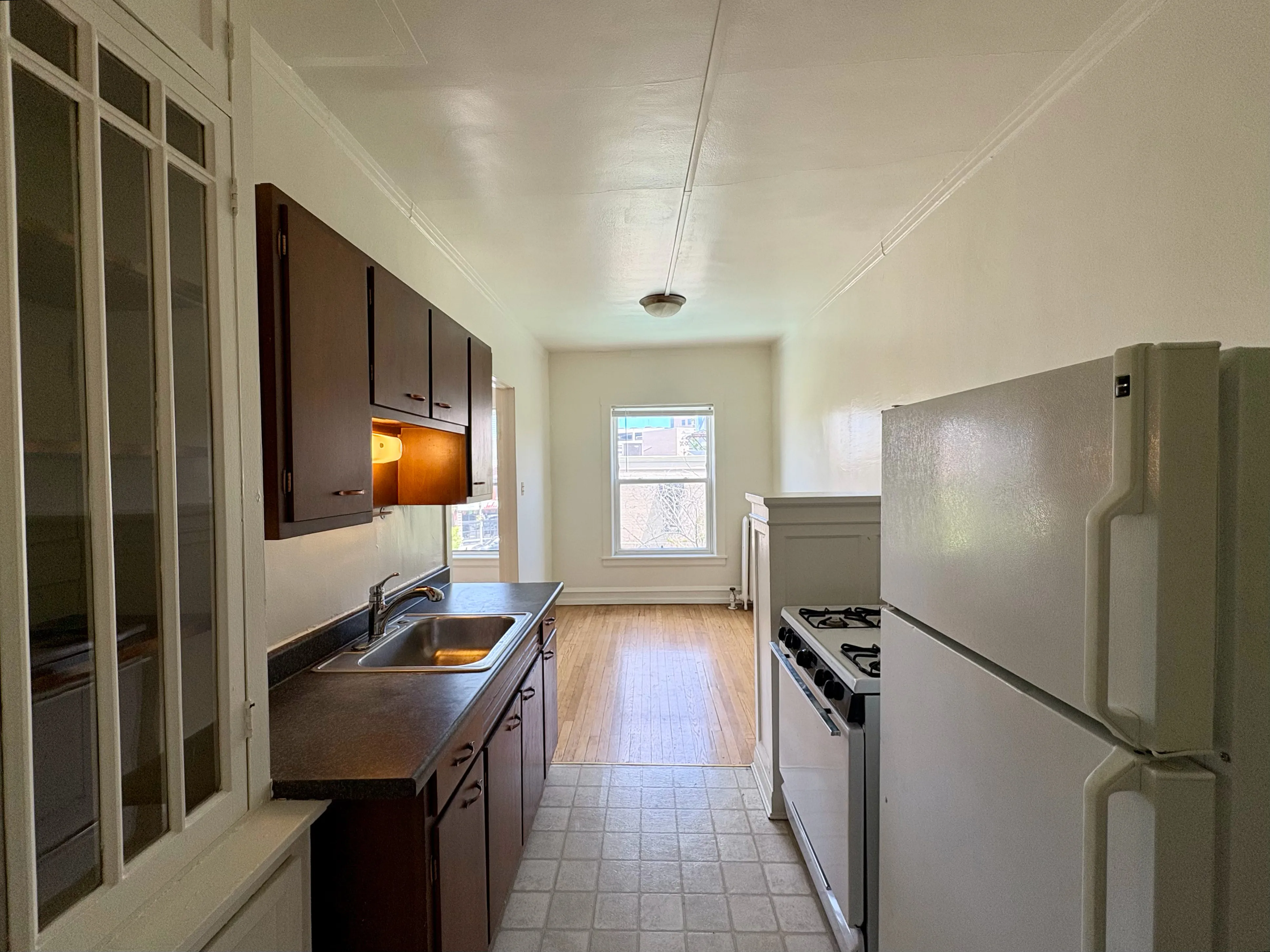 Bright kitchen with modern dark wood cabinets, large window, and sleek appliances, offering a cozy cooking space.
