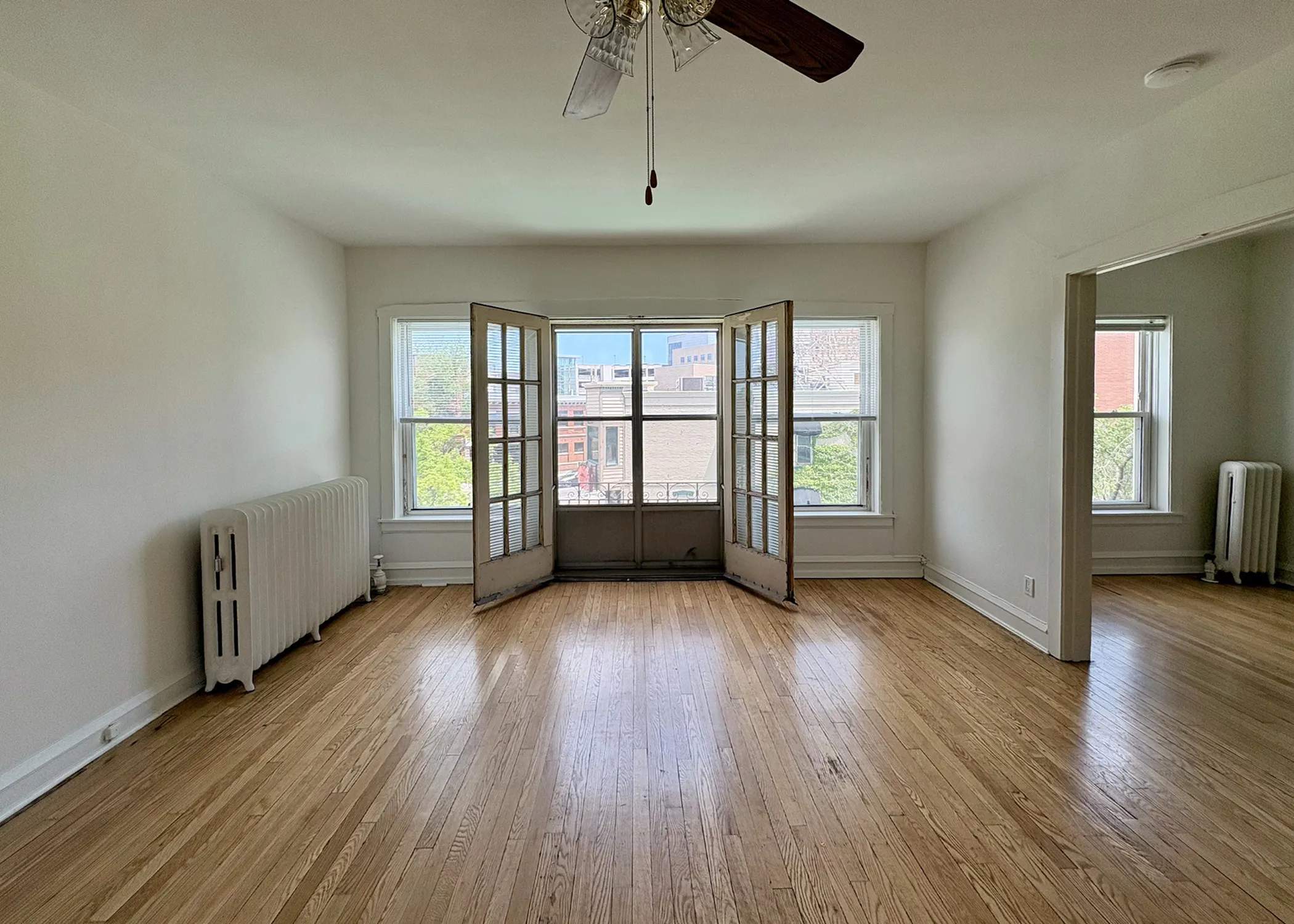 Bright and spacious apartment with elegant hardwood floors, large windows, and charming French doors opening to a city view.