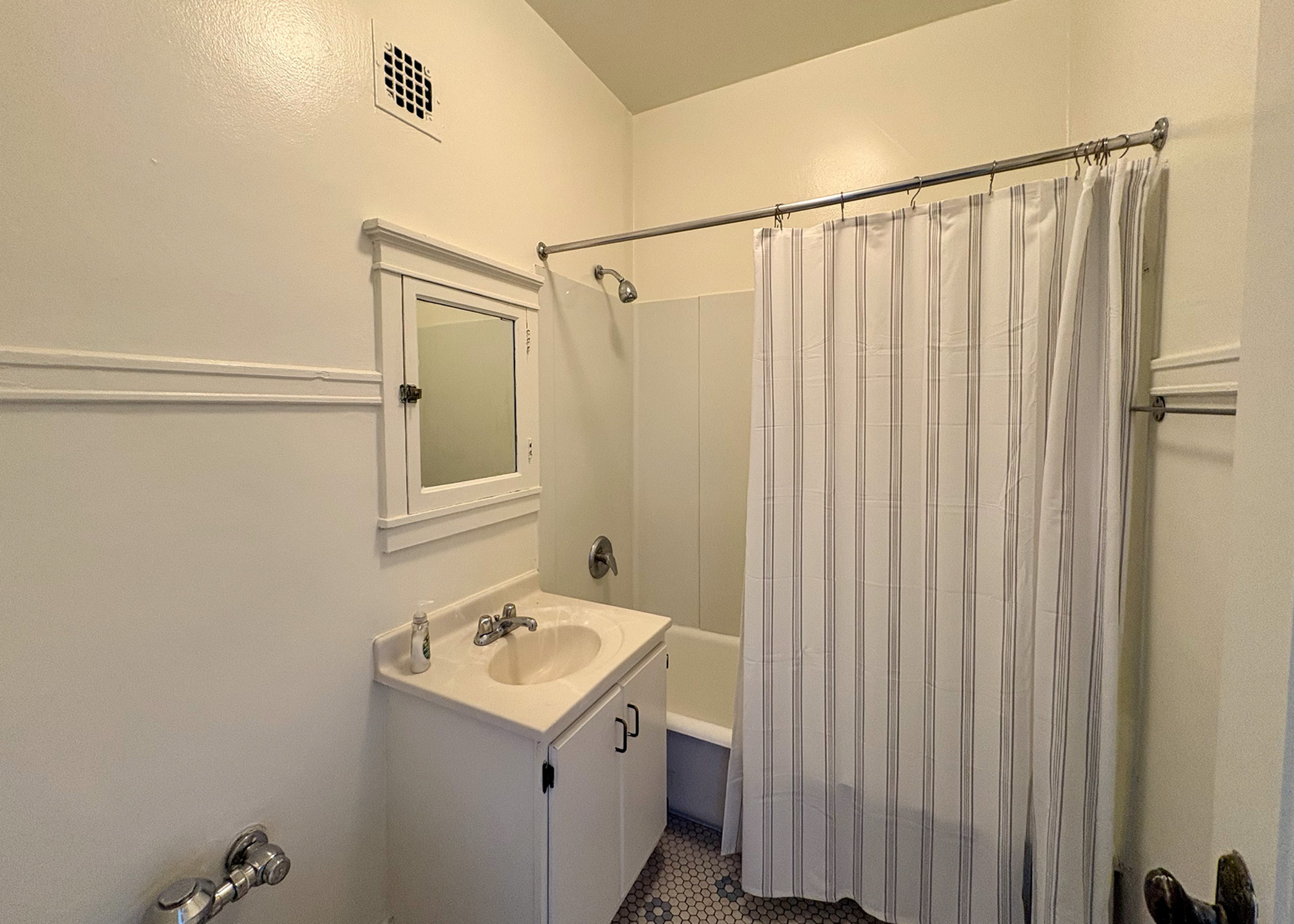 Cozy and bright bathroom with classic white design, featuring a stylish shower curtain, vintage tile flooring, and elegant vanity mirror for a timeless feel.