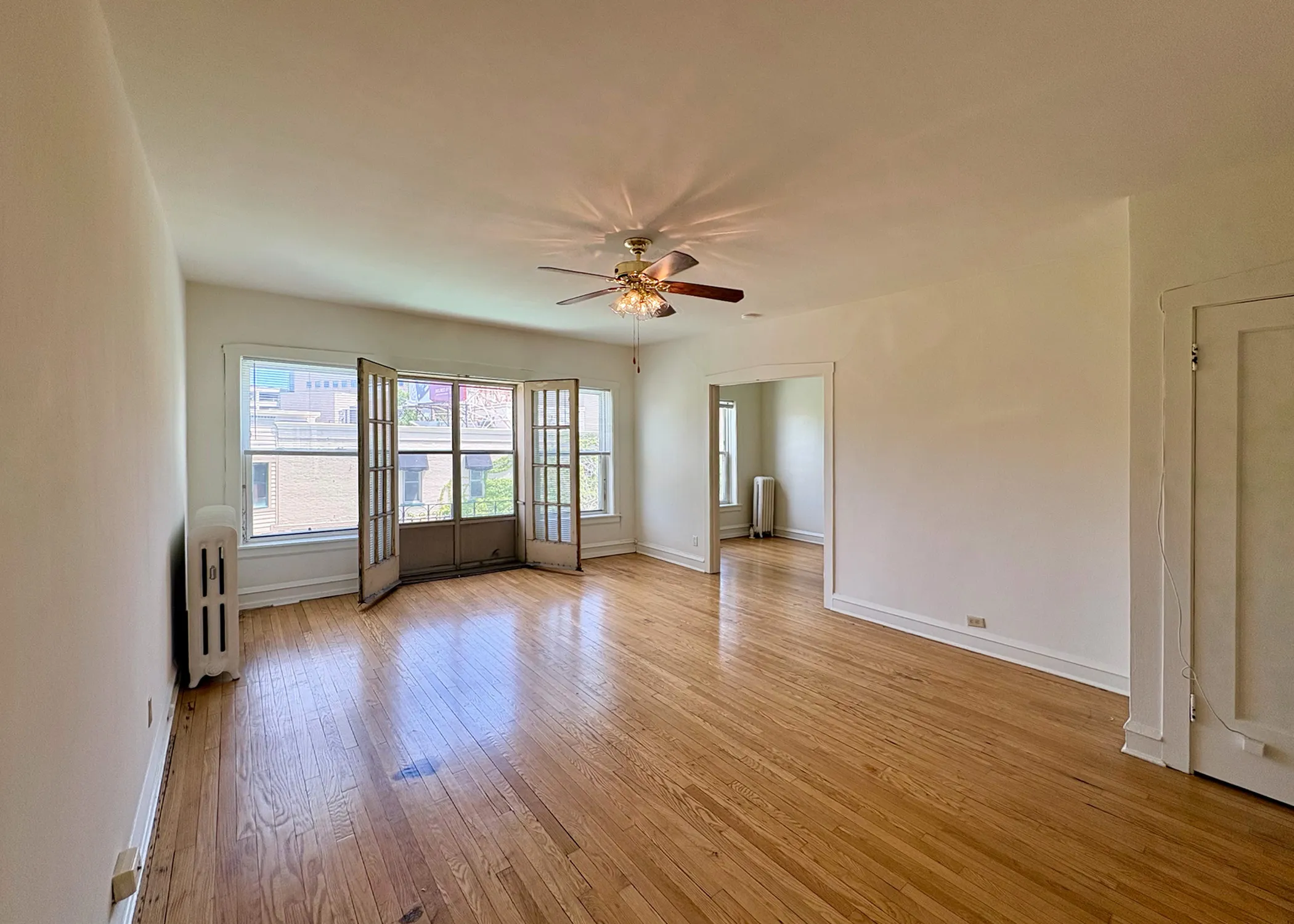 Bright and spacious living room with elegant hardwood floors, large windows, and a ceiling fan for optimal comfort.