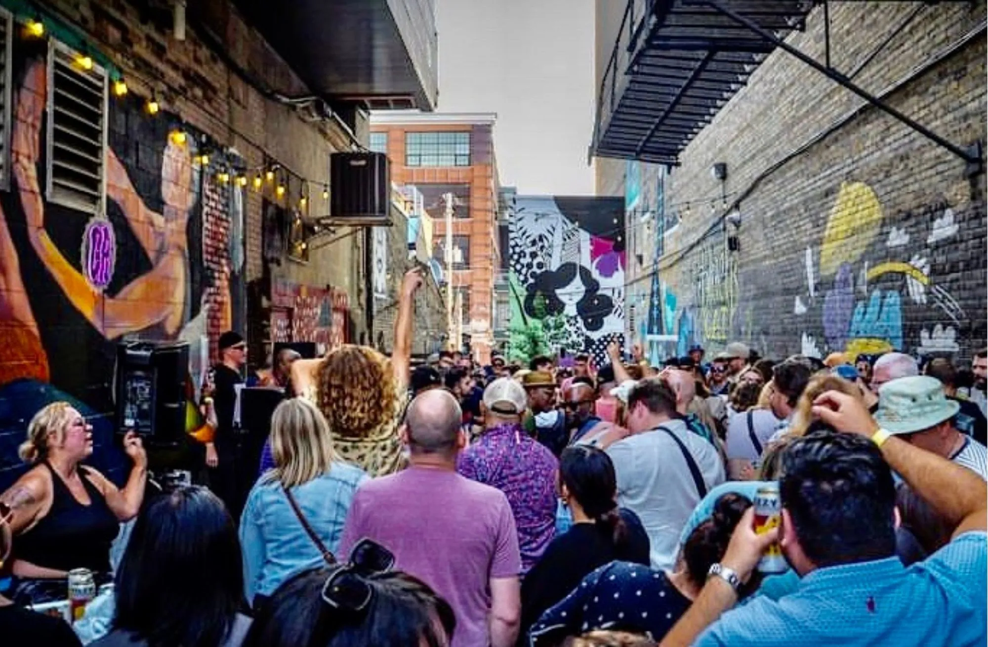 Vibrant outdoor urban gathering with colorful street art and a lively crowd enjoying a festival atmosphere.
