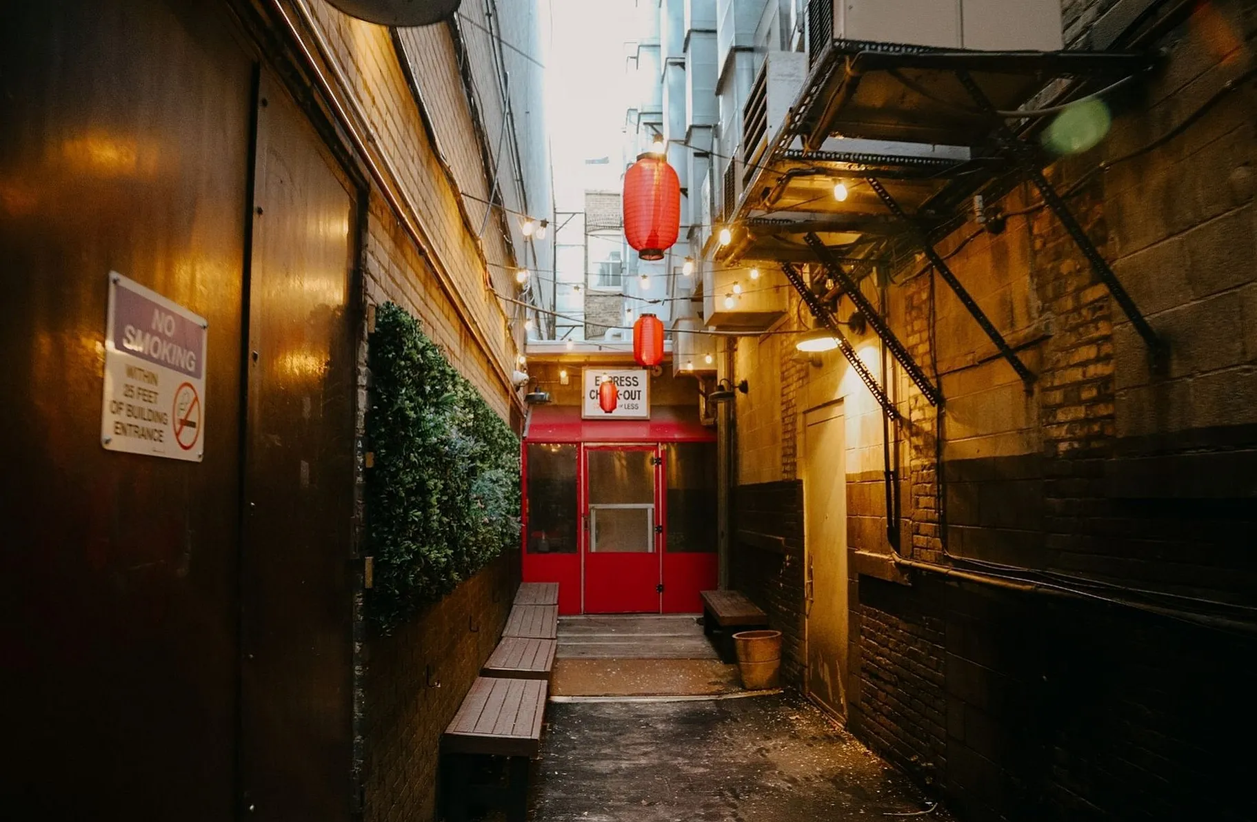 Charming urban alley featuring cozy string lights and vibrant red lanterns leading to an inviting express checkout doorway.