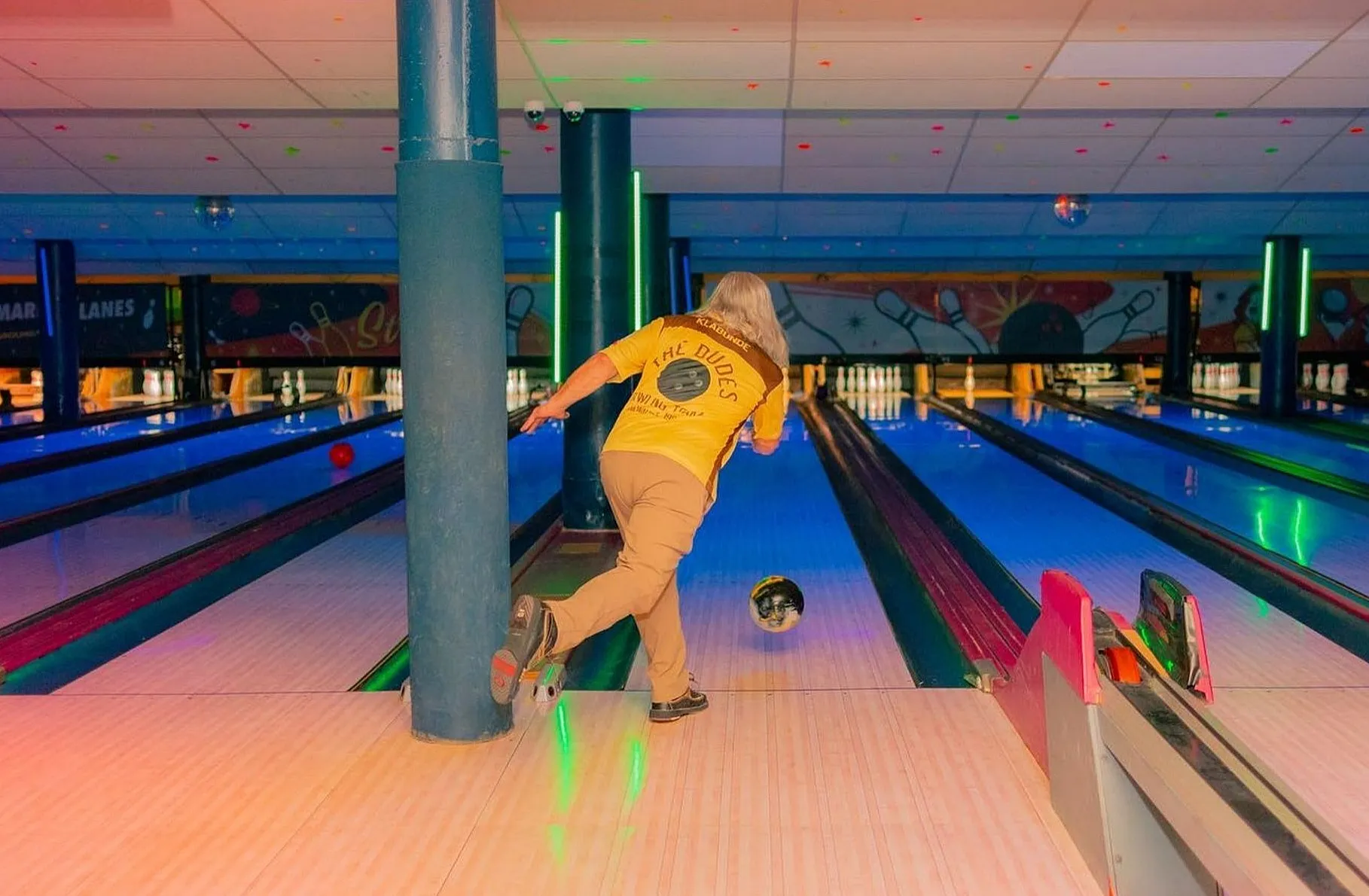 Dynamic view of a vibrant bowling alley with a player in motion, capturing the excitement of bowling under colorful lights.