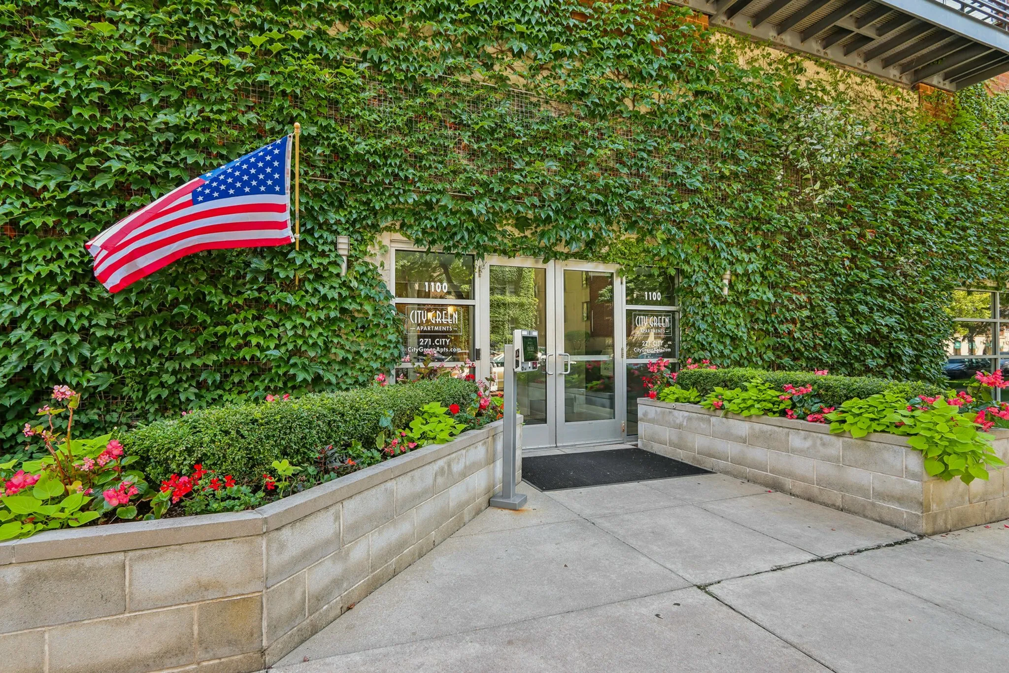 Inviting entrance of City Green Apartments, adorned with lush ivy and vibrant flower beds, showcasing a welcoming and serene atmosphere.