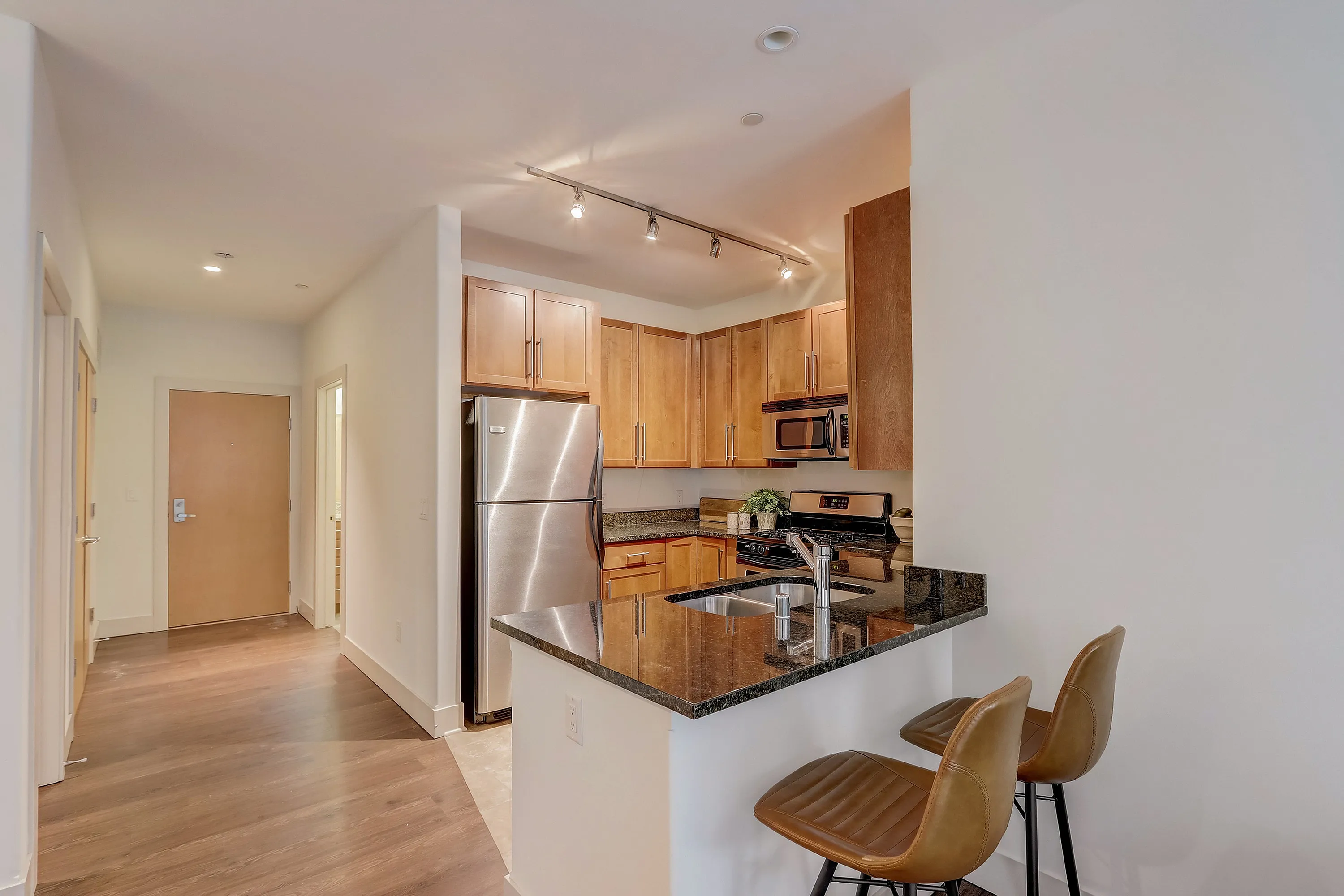 Modern kitchen with stainless steel appliances, granite countertops, and stylish wooden cabinets featuring chic bar seating.