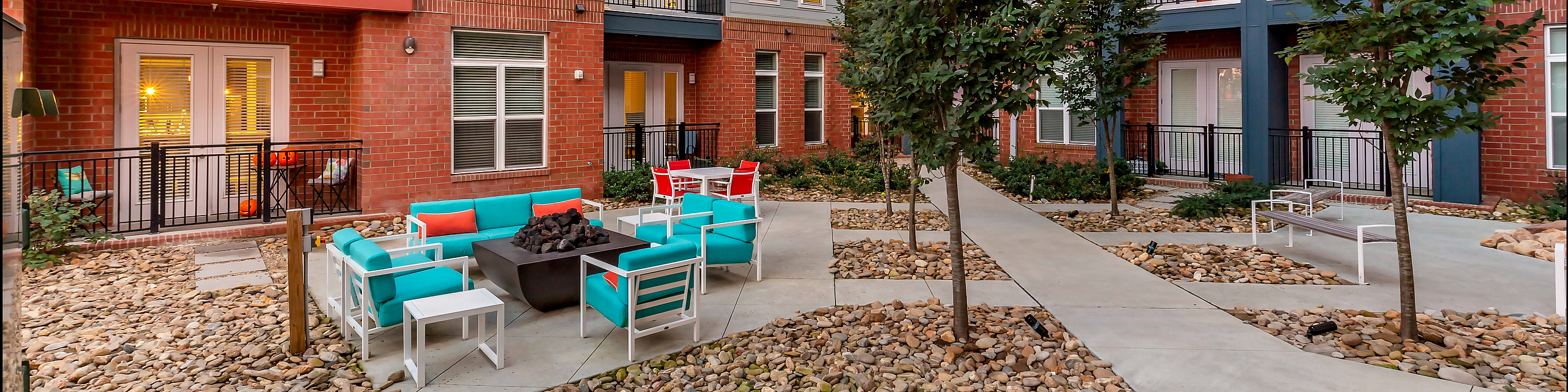 Chic apartment courtyard with colorful seating area, surrounded by modern balconies and lush greenery.