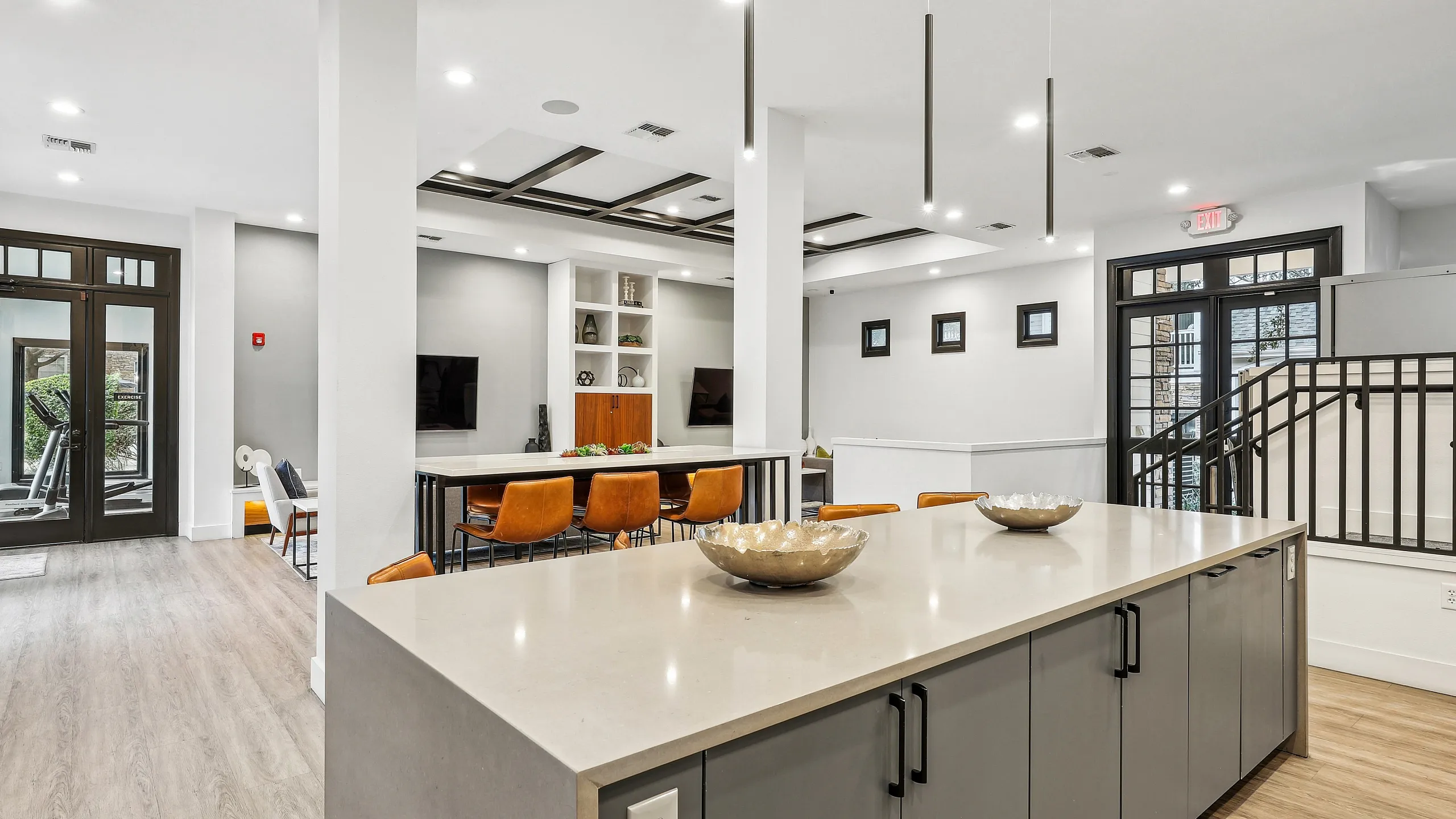 Modern communal space featuring sleek kitchen island, leather chairs, and stylish dining area with abundant natural light.