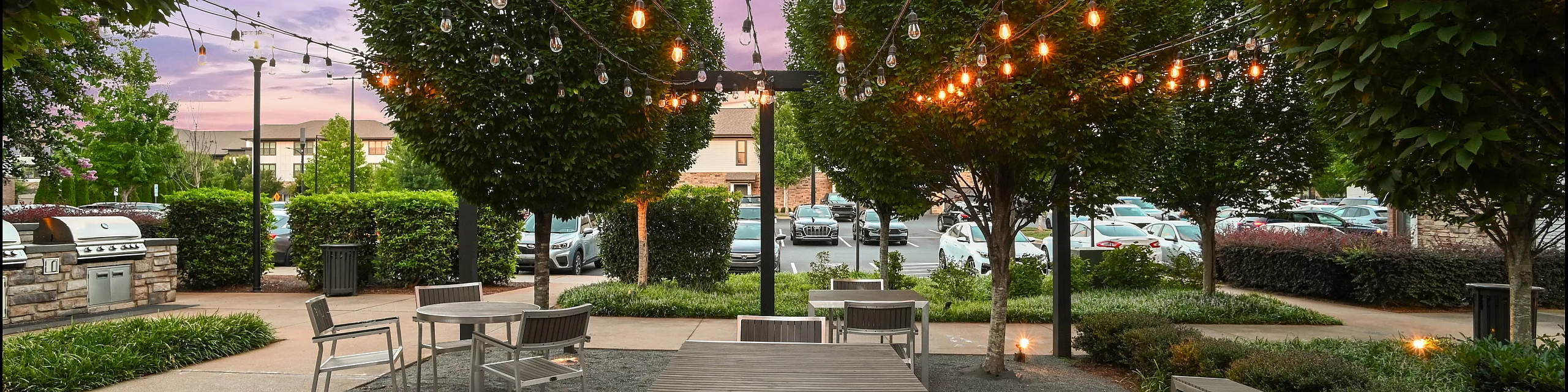 Charming outdoor patio with string lights draped over modern seating, surrounded by lush greenery and equipped with a barbecue area for entertaining.