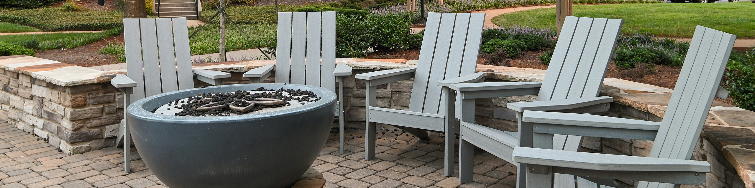 Charming outdoor seating area with stylish Adirondack chairs surrounding a modern fire pit, set against lush greenery and elegant stone pathways.