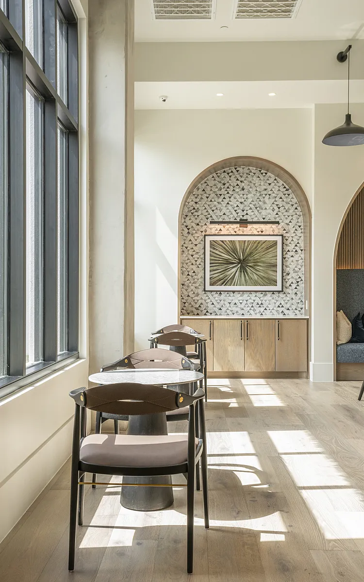 Bright and elegant dining area with stylish wooden chairs, chic marble tables, and a decorative feature wall, flooded with natural light from large windows.